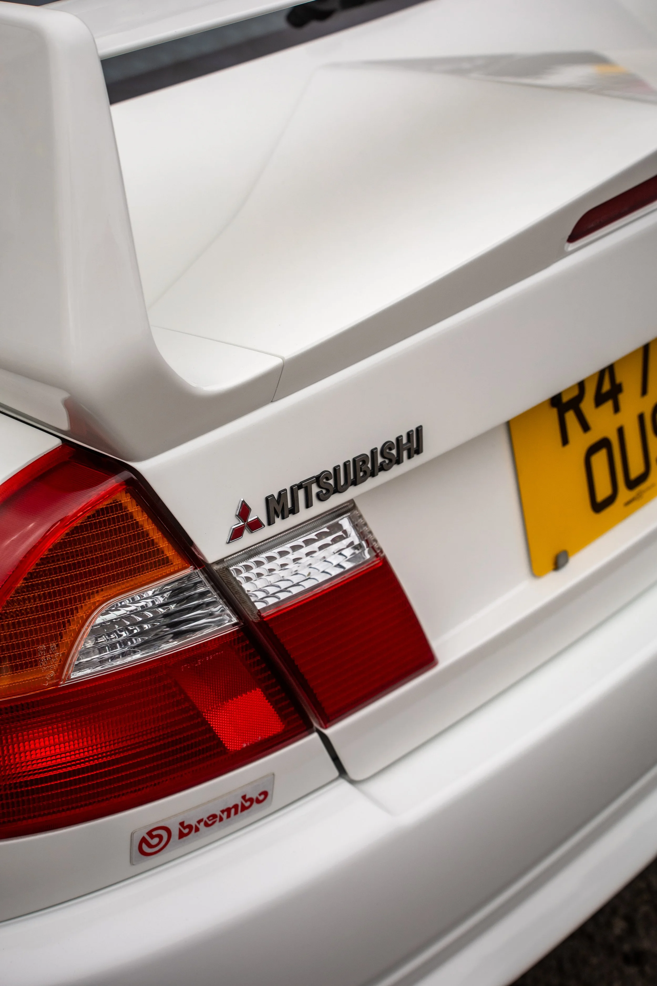 Close-up of the rear of a white Mitsubishi car showing its tail light, Mitsubishi emblem, and a Bremo brake sticker.
