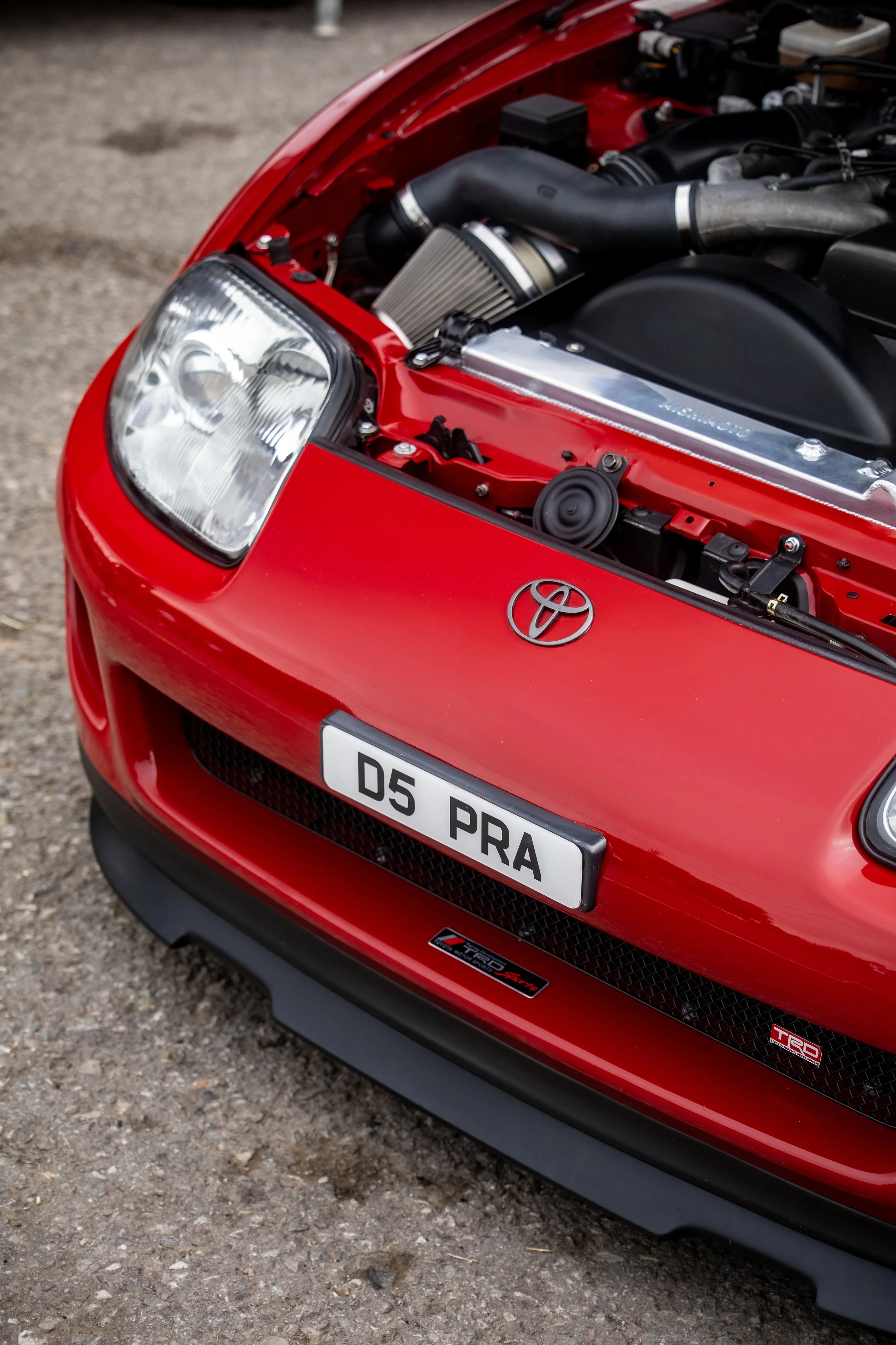 Front view of a red Toyota race car with an open hood showing the engine, featuring a Toyota emblem and a license plate reading 'D5 PRA'.