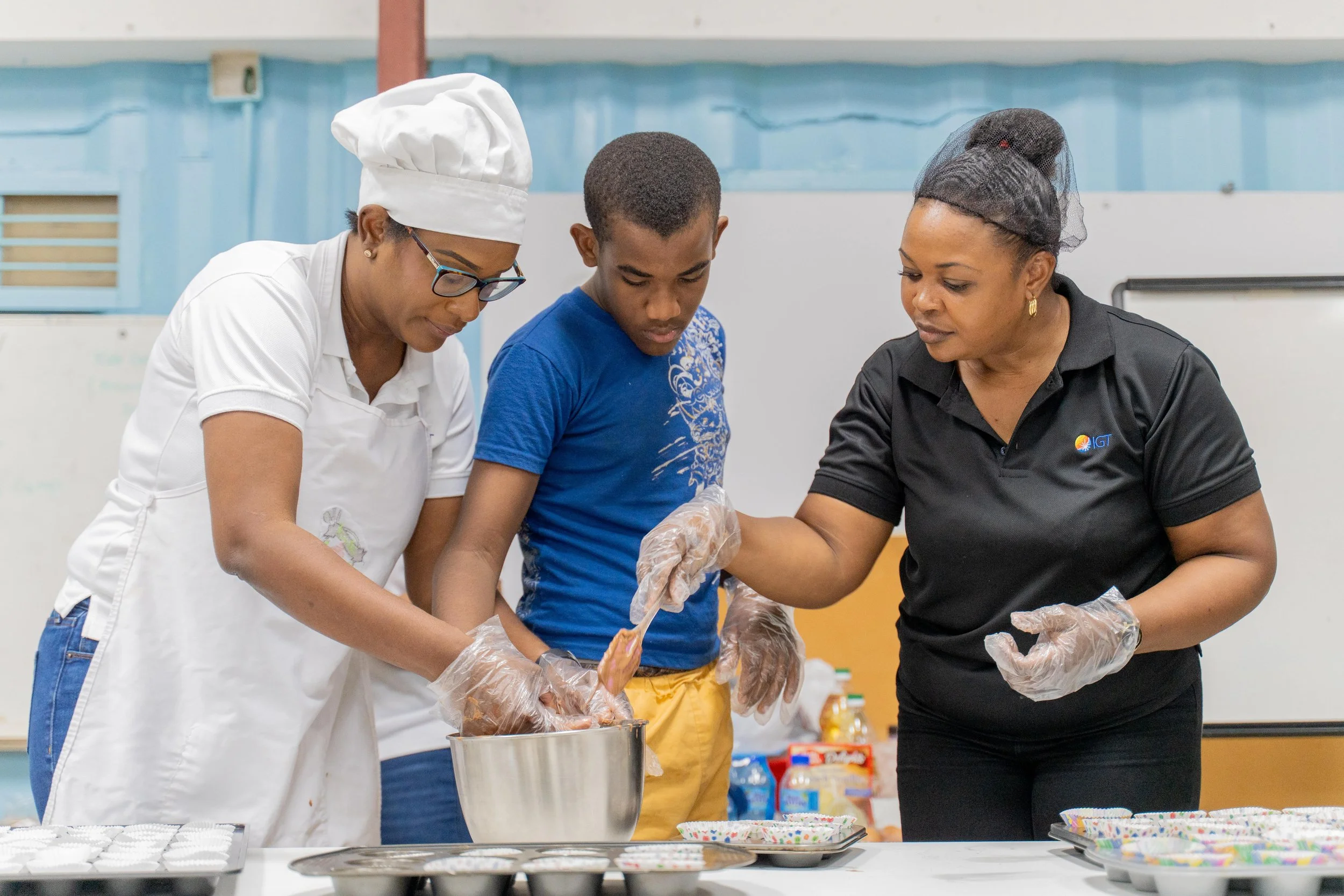 Stirring up smiles and sweet moments: Jeran Romero (centre) joins IGT employees Cherisse Charles (left) and Rowen Marshall (right) in baking cupcakes on 16th May at Autism Place in D’Abadie.