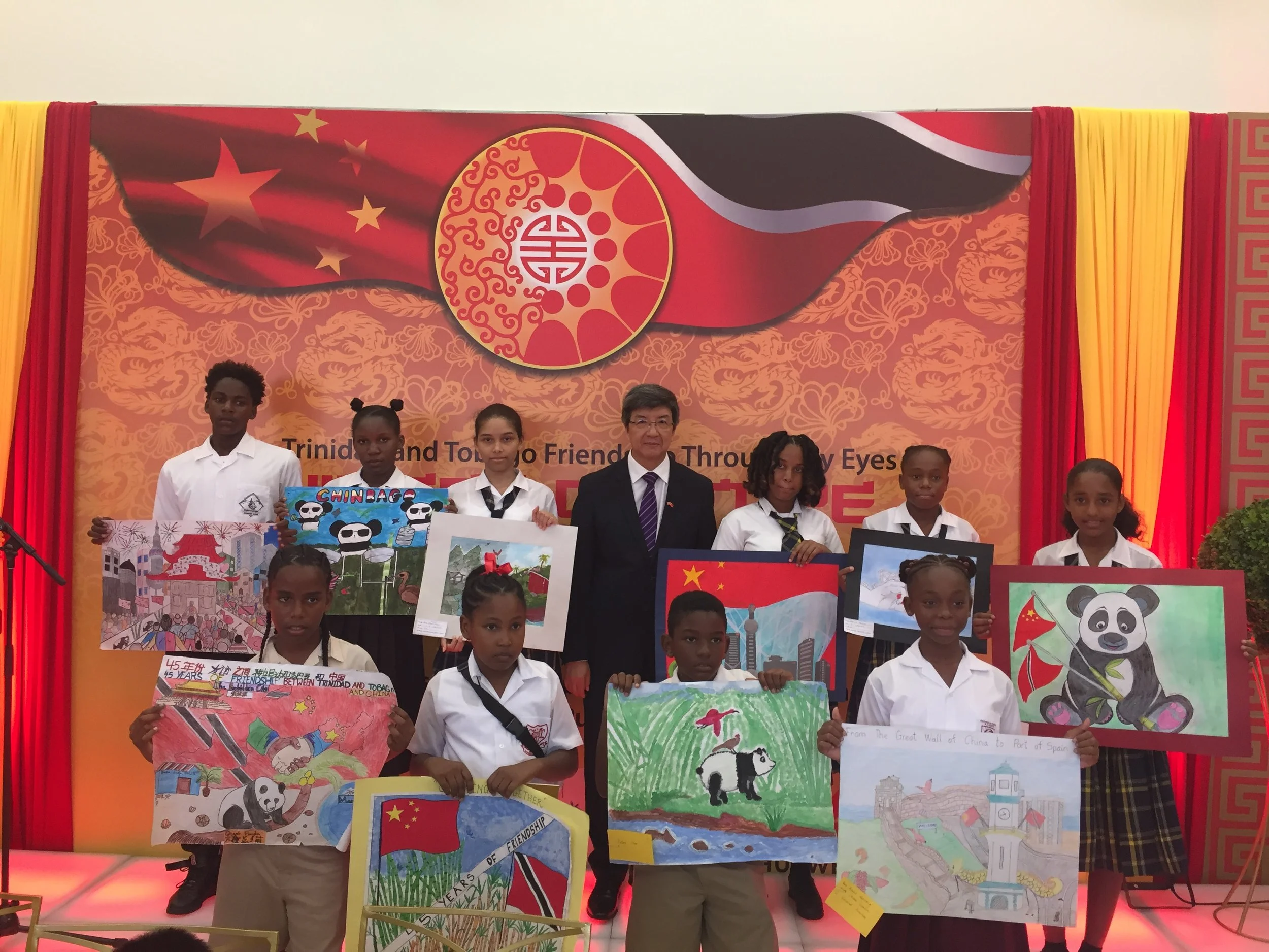  Chinese Ambassador Song Yumin stands with Mayaro students who received special awards for their art pieces at the Arts Award Ceremony: China-Trinidad and Tobago Friendship Through My Eyes in 2019, following sponsorship of ongoing initiatives for the Mayaro community supported by SWF&CO.  