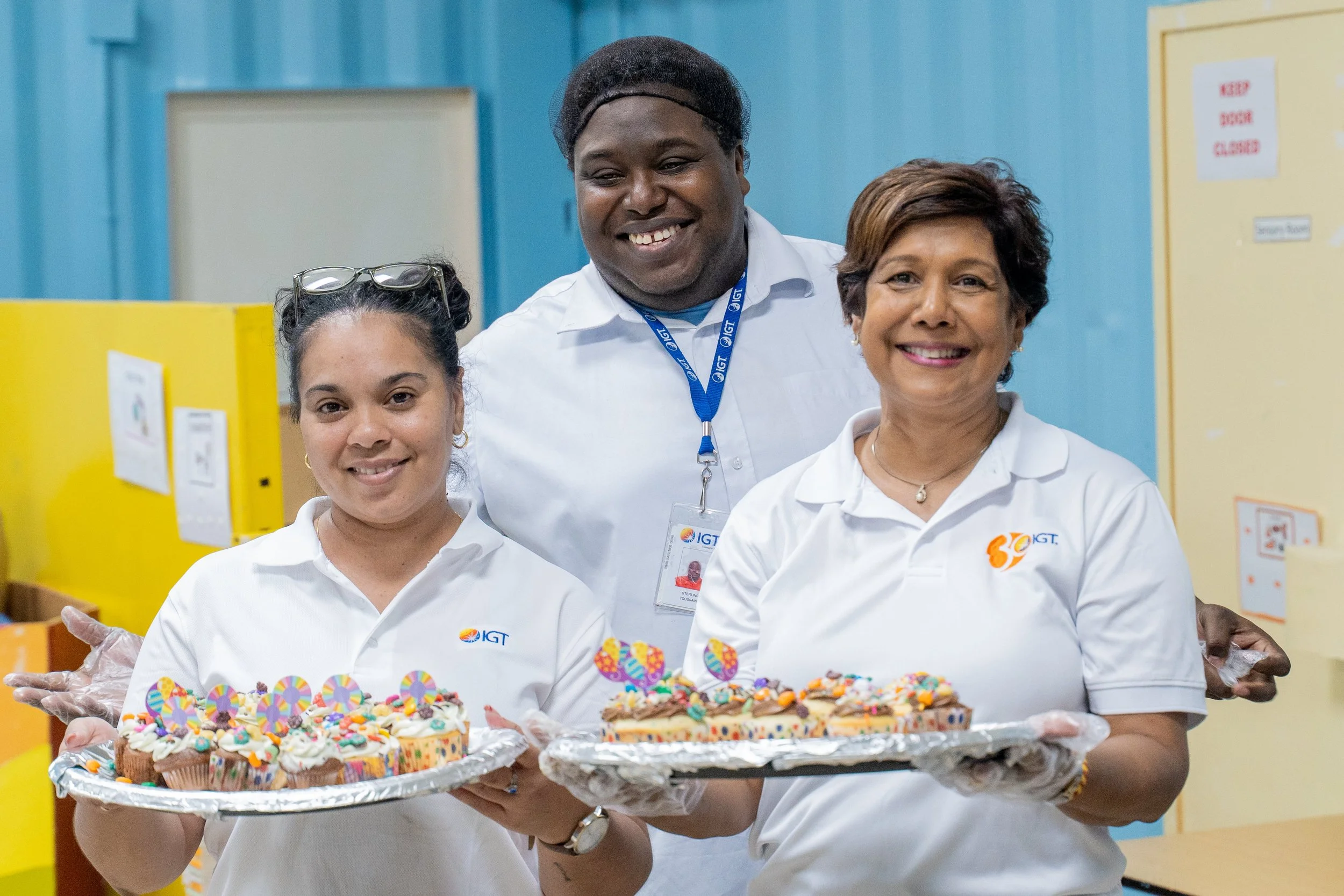 IGT Global Giving Month Volunteers Laura Da’Breau, Strategic Accounts Associate, Sterling Toussaint, IGT Procall Representative, and Shavindra Tewarie-Singh, IGT People & Transformation Regional Senior Manager for the Caribbean, display cupcakes decorated by the ASTT adult recreation group at Autism Place, D’Abadie, on 16th May.