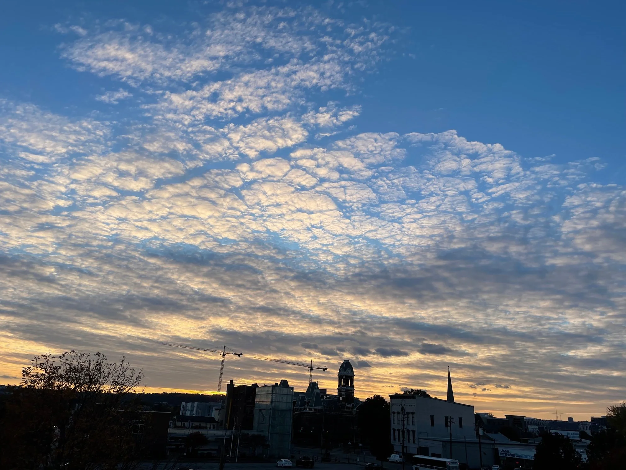 City skyline at sunset with a partly cloudy sky, construction cranes, and historic buildings.