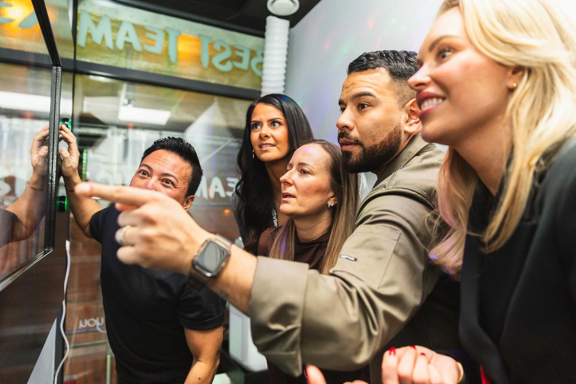 Grupp människor tittar och pekar på en skärm eller affisch i ett butik eller café, med texten 'BESTREAM' synlig i bakgrunden.