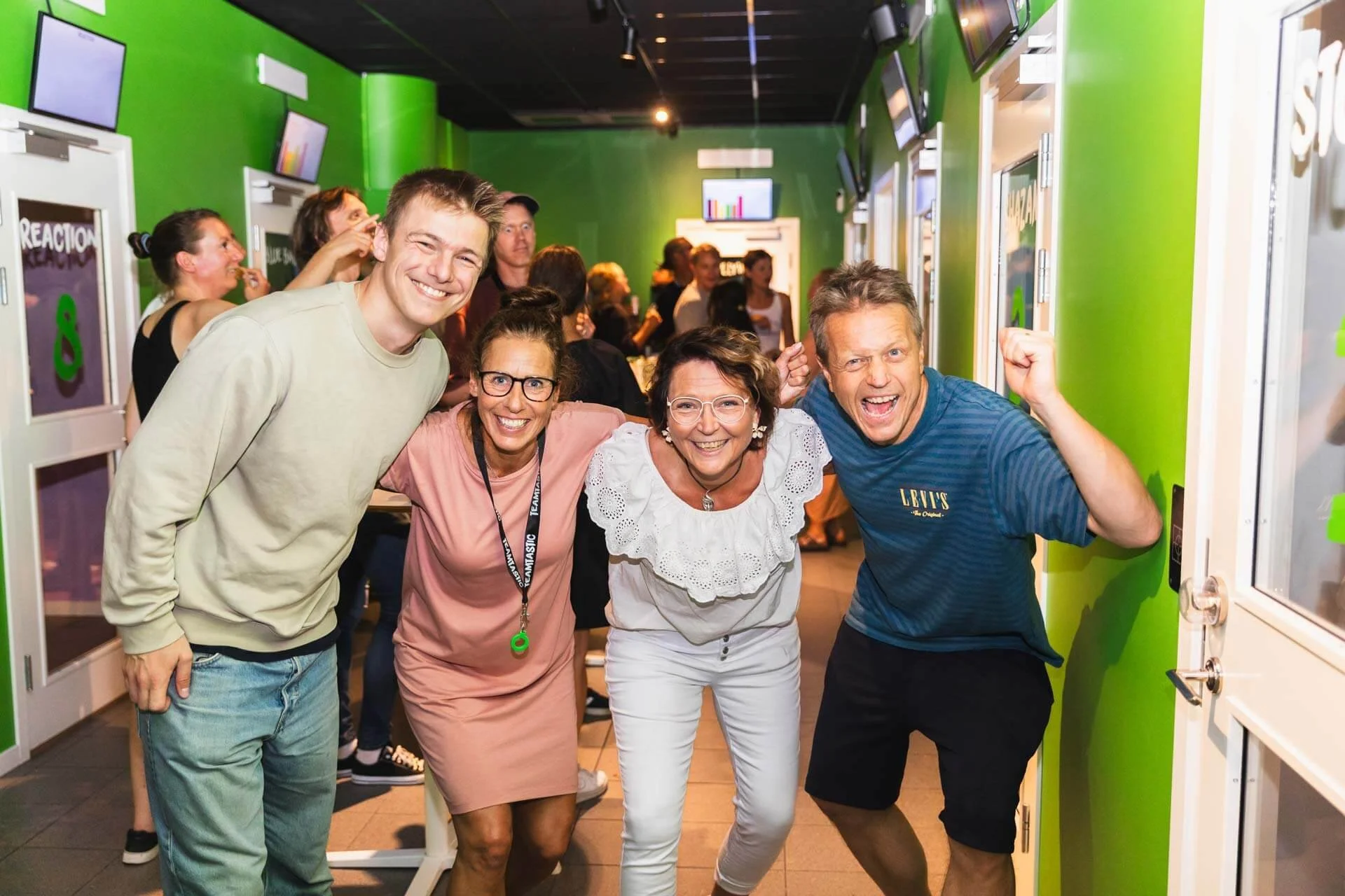 Grupp av fyra personer som ler och firar, står nära varandra framför en grön vägg på en fest eller social sammankomst.