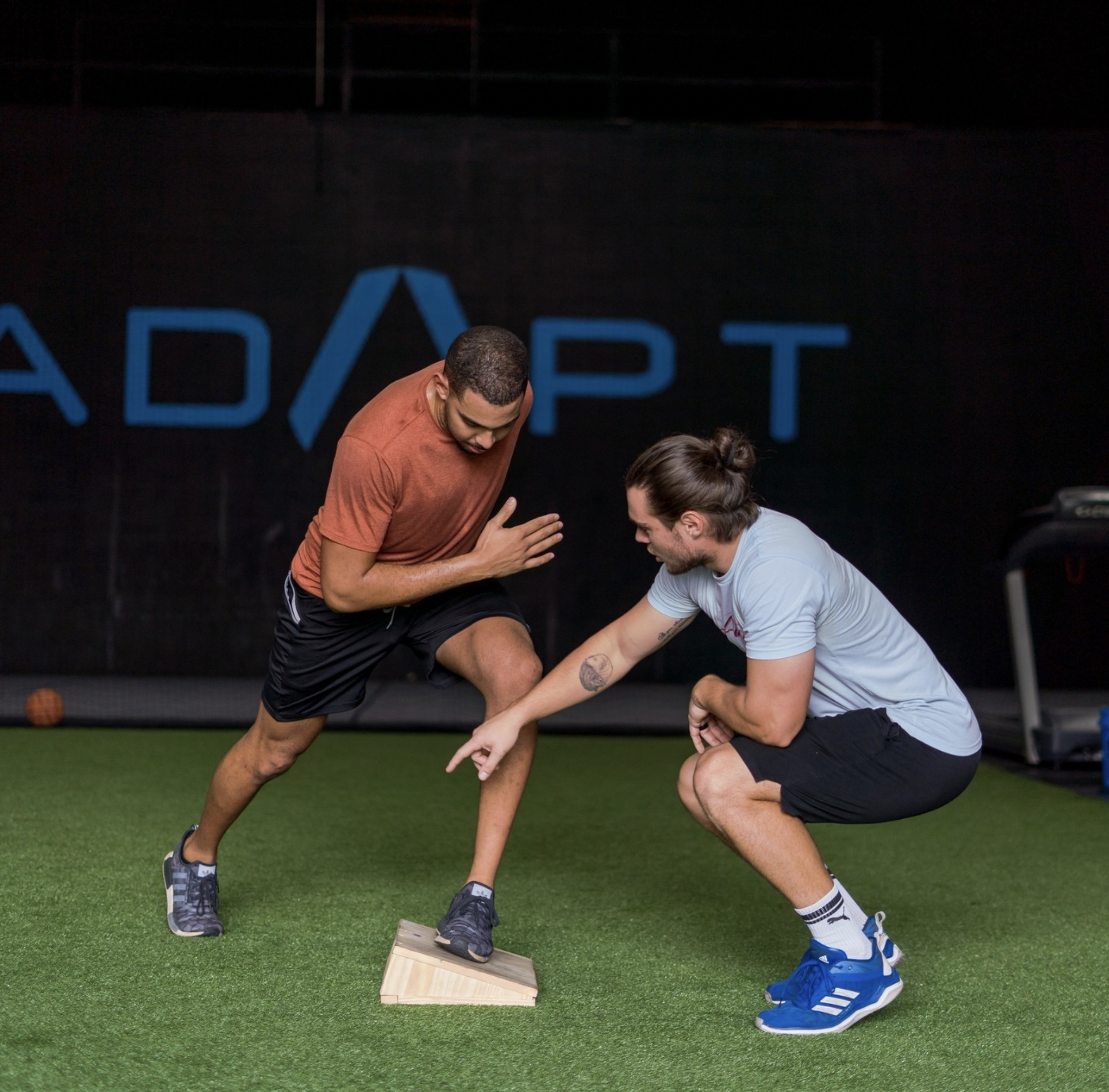 Personal trainer and client practicing agility drill with a wedge trainer on artificial turf at a gym