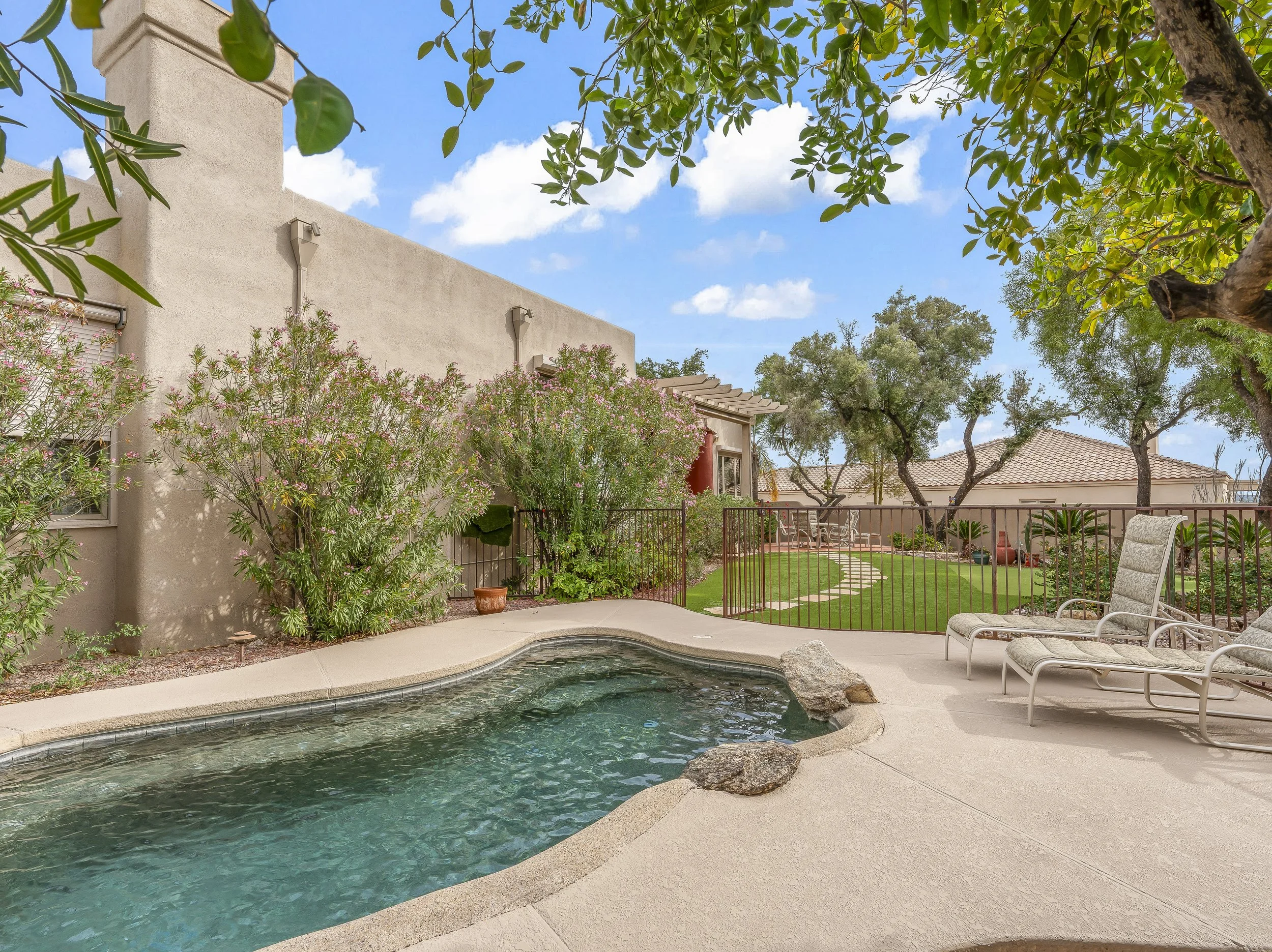 Resort-style backyard at 3825 Mountain Cove Dr featuring a freeform heated pool with natural rock waterfall, separate spa, safety fencing, and mature landscaping in the Catalina Foothills.