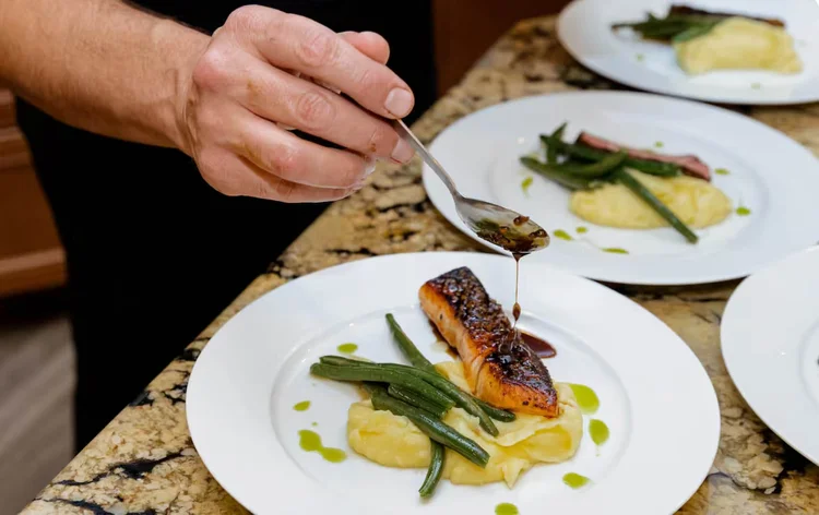 Chef plating salmon with vegetables and sauce
