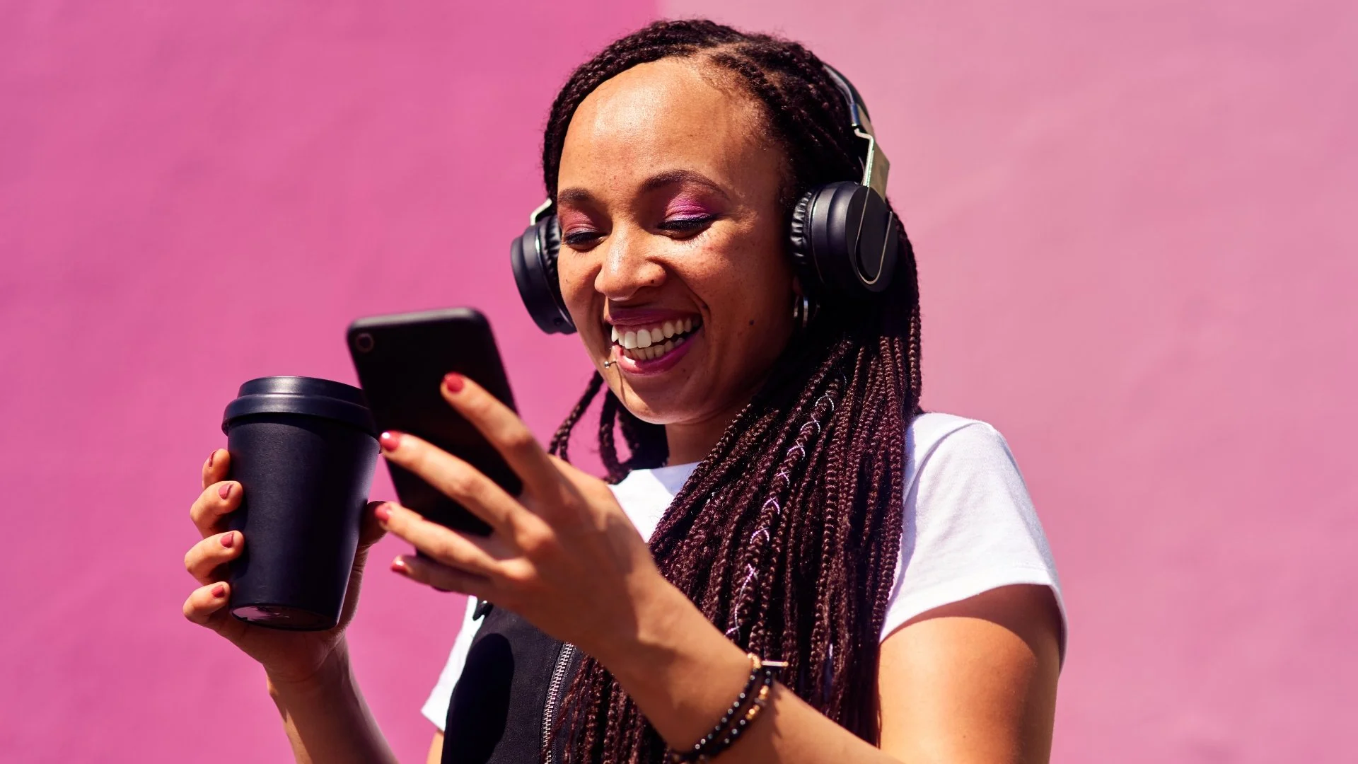 A nonprofit social media manager smiling at their phone and holding a cup of coffee while checking posts scheduled with their social media scheduling tool