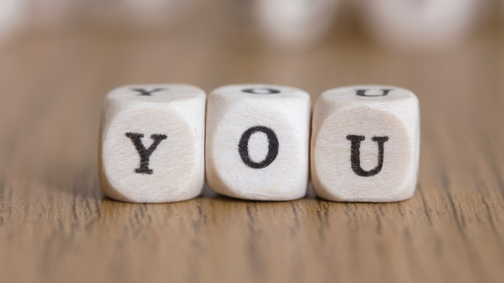Three wooden letter dice spelling the word "YOU" on a wood surface