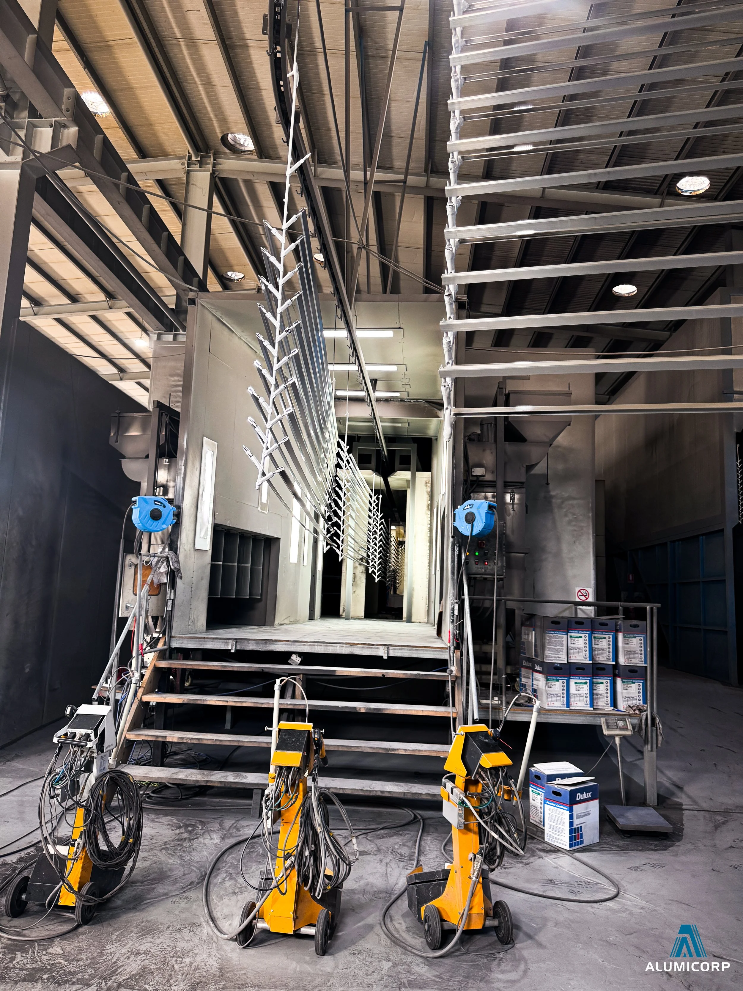 Industrial kitchen or food processing facility with metallic stairs, large metallic containers, and blue machinery. The floor is concrete, and there are various wires and equipment related to industrial food prep or processing.