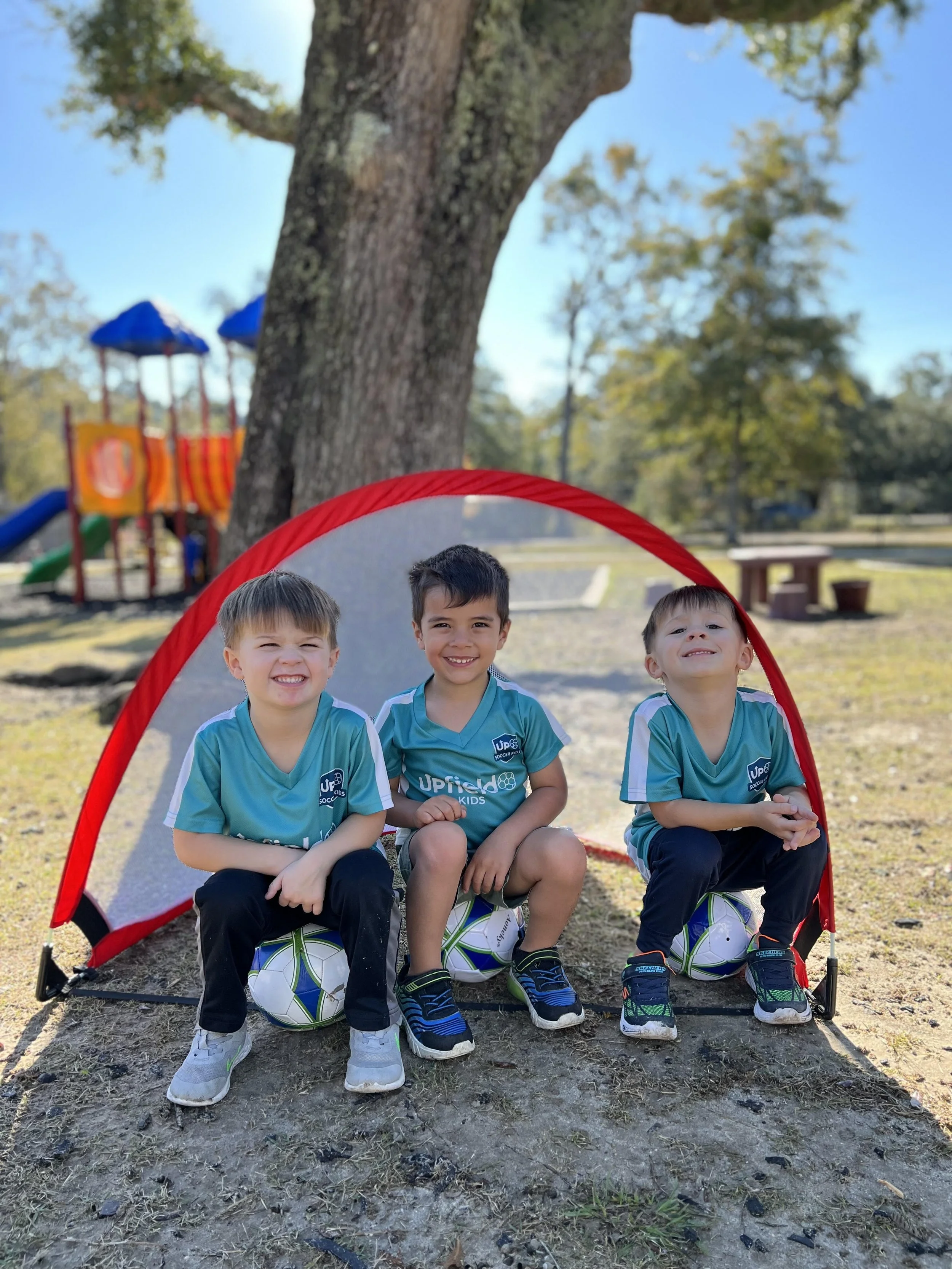 toddlers sit on top of soccer balls in front of a pop up soccer goal