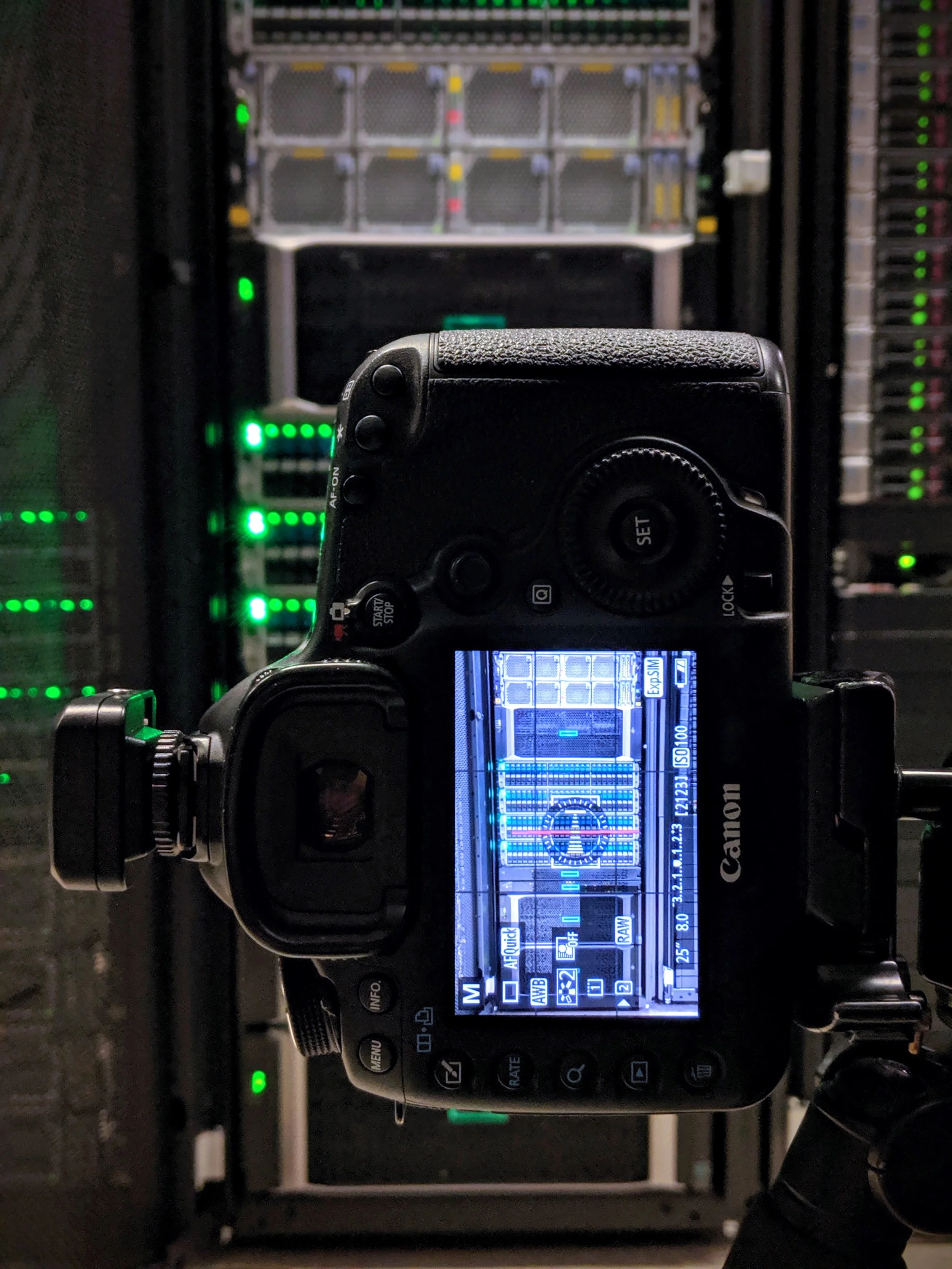 Close-up of a Canon DSLR camera mounted on a tripod, capturing images of a server rack with illuminated green and yellow indicator lights.