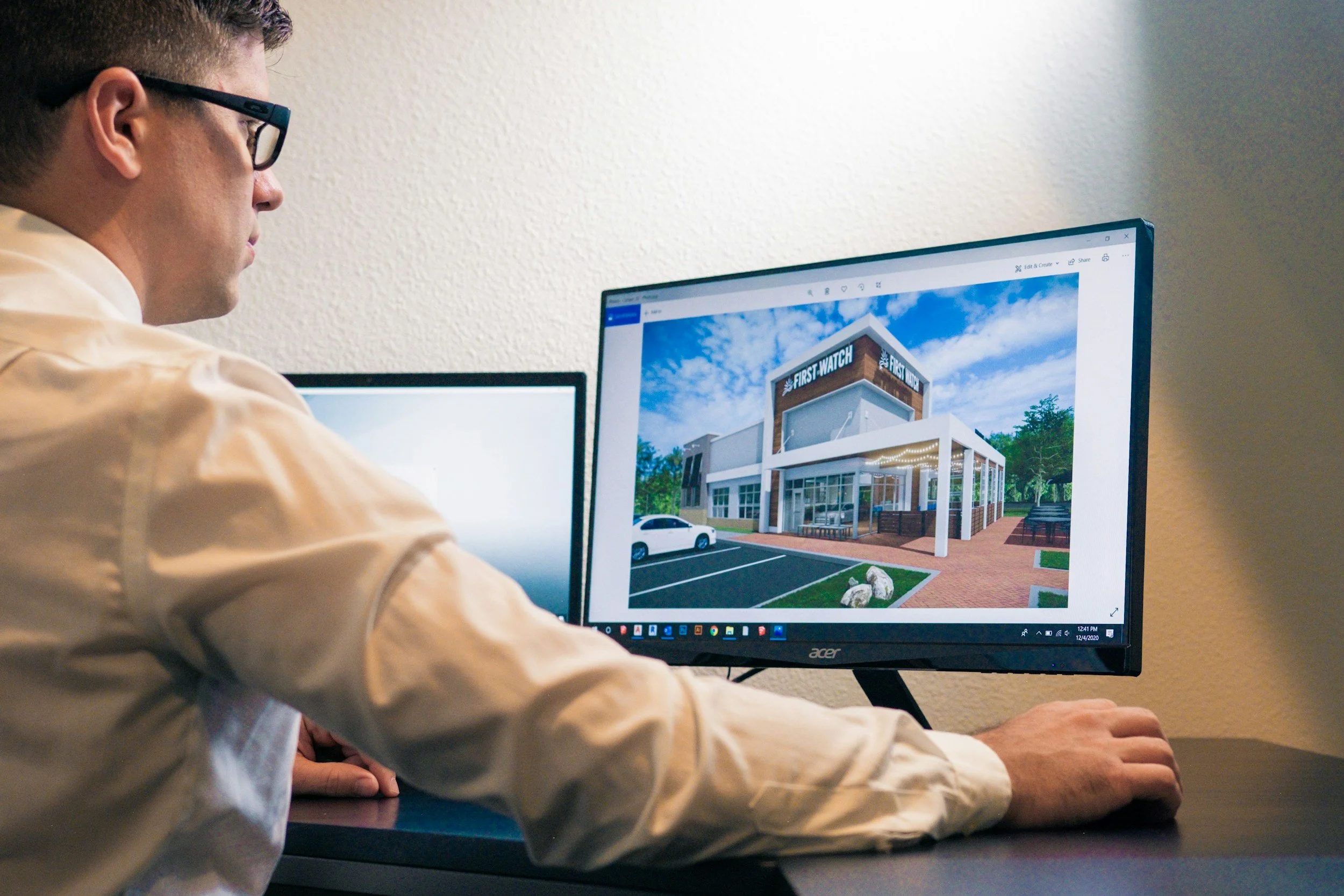 A person with glasses wearing a light-colored shirt working on a computer with a building project visible on the screen.