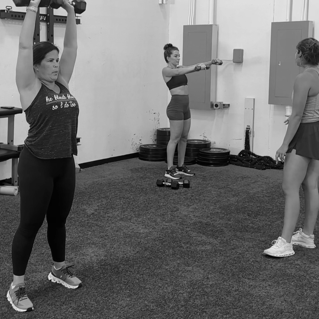 A man with curly dark hair, glasses, and a beard, smiling softly, wearing a dark sweater, with a plant in the background.