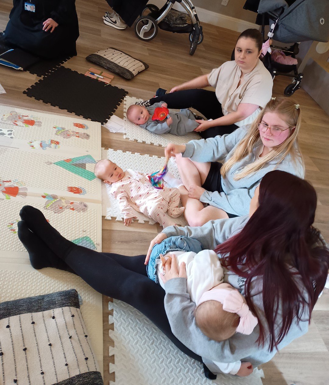 Three women sitting on the floor with babies on a playmat
