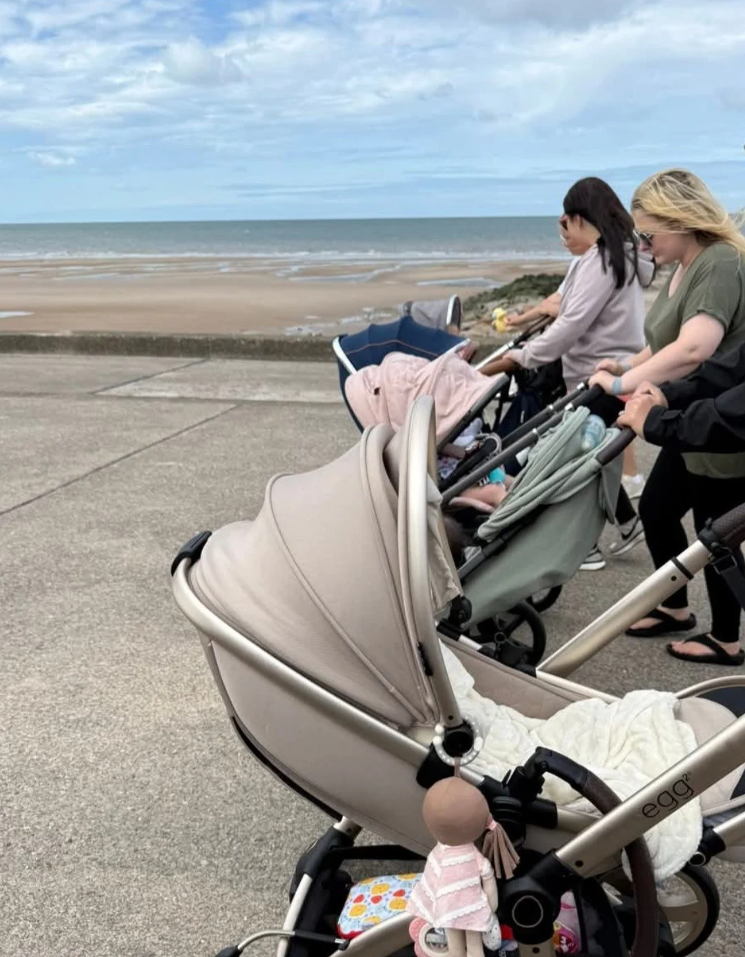 Three buggies being pushed along a path with a beach in the background