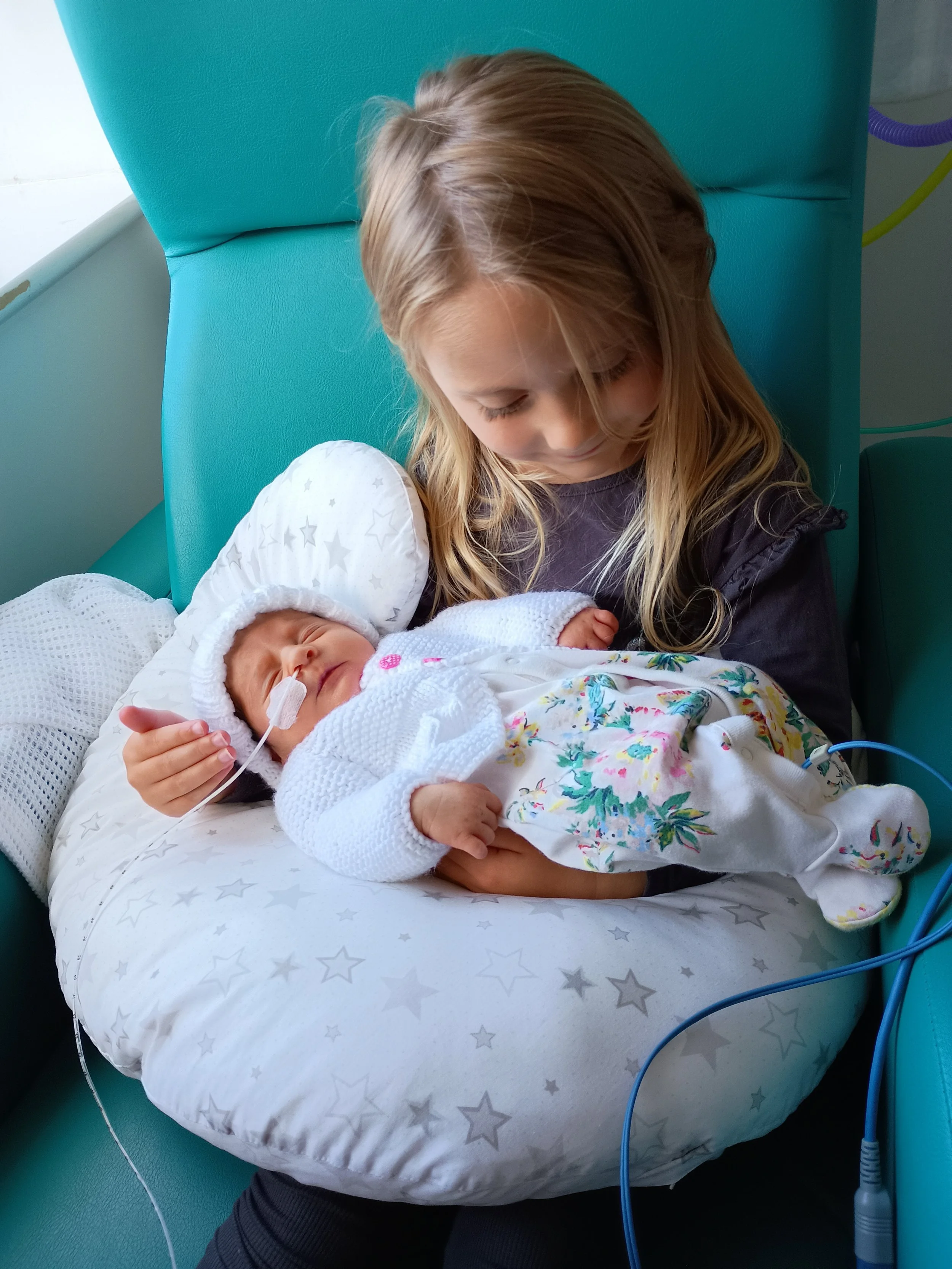 Young girl holding baby with feeding tube on a pillow on her lap.