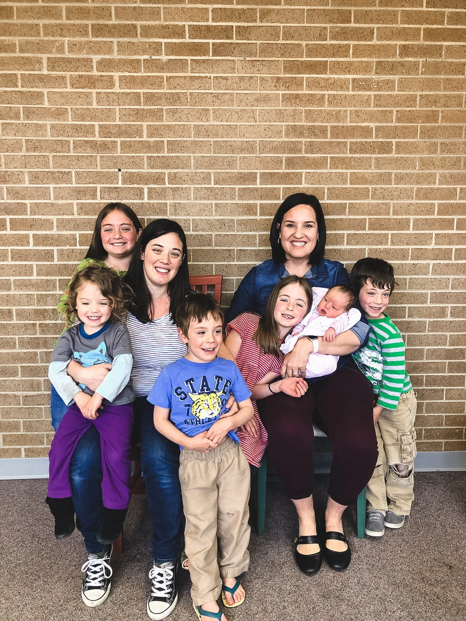 Group photo of two women sitting with five children against a brick wall. Featuring Kattie Jones, a Spanish speaking midwife in denver co