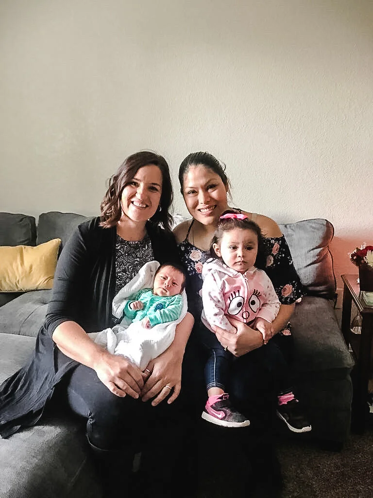 Two women, one of them being kattie jones, sitting on a couch with a baby and a young girl, smiling at the camera. Both happy after Home birth