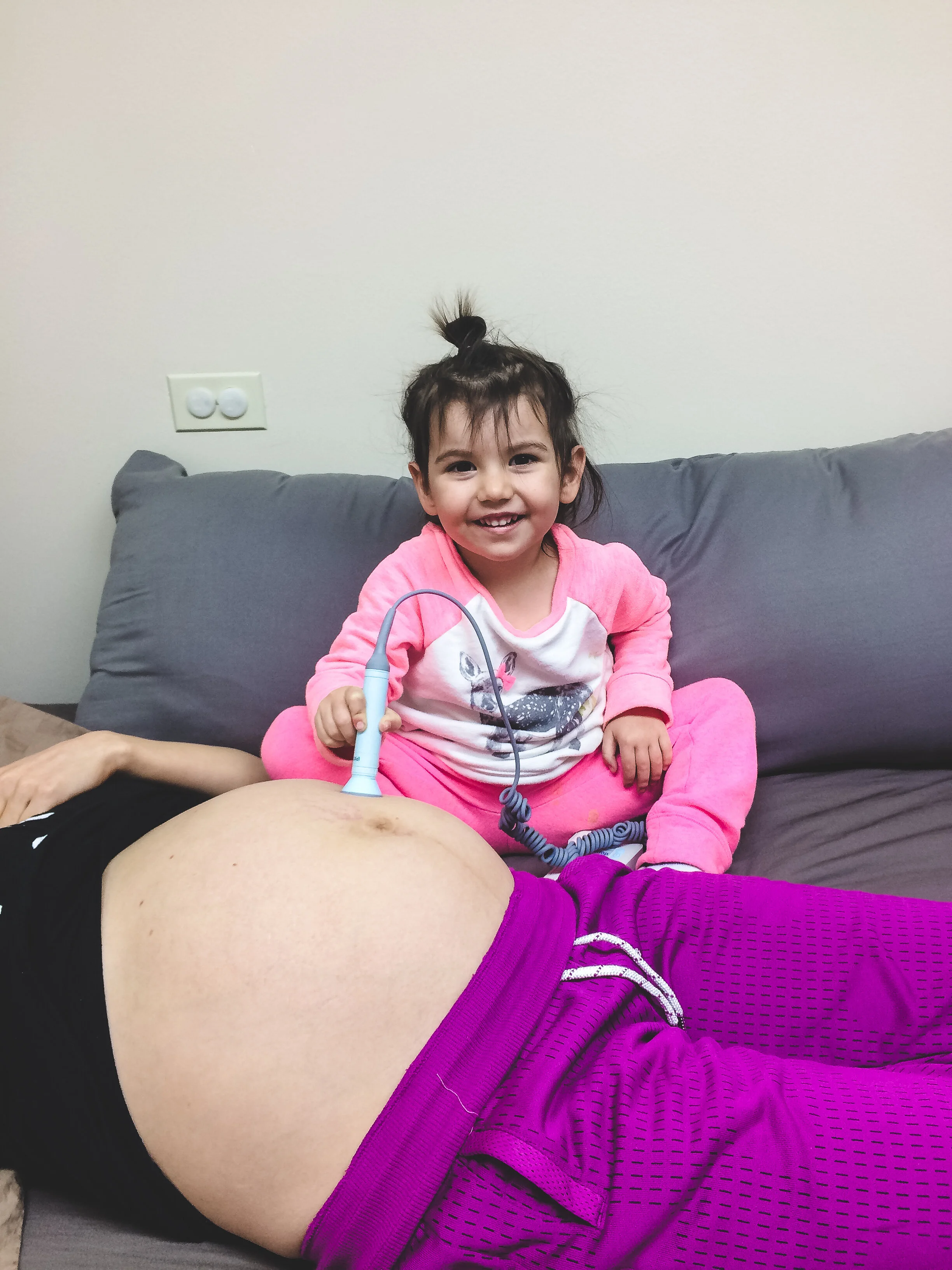 Little girl using a toy stethoscope on a pregnant belly, smiling.