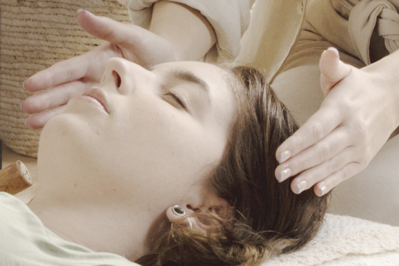 reclined woman with practitioners hands near head receiving reiki treatment