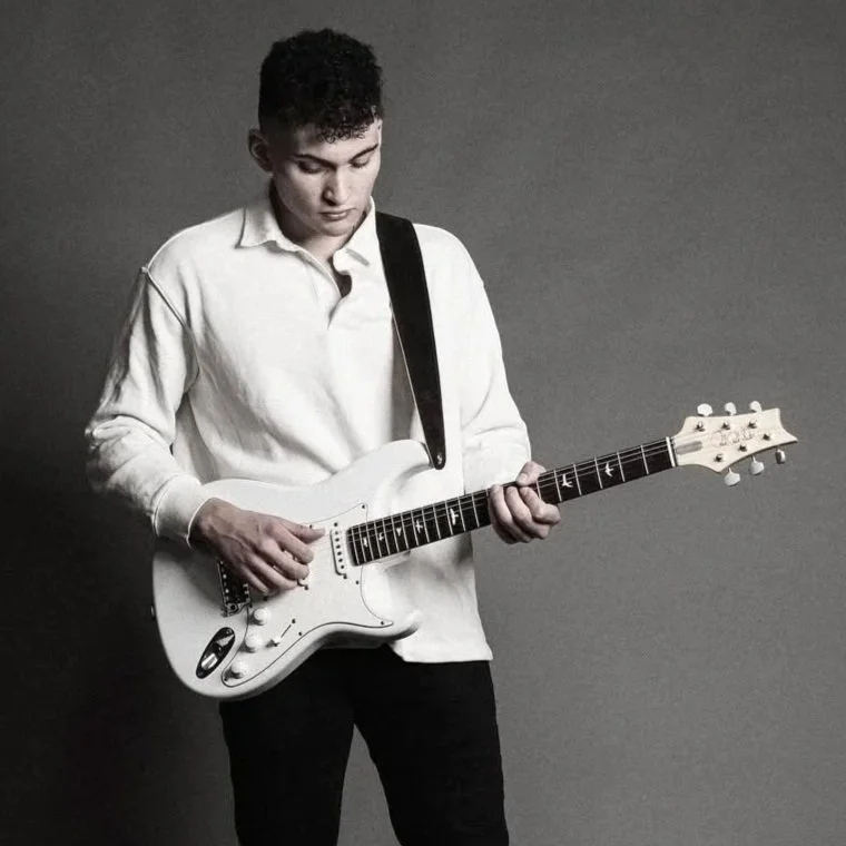 Young man in a white shirt playing an electric guitar against a plain grey background.