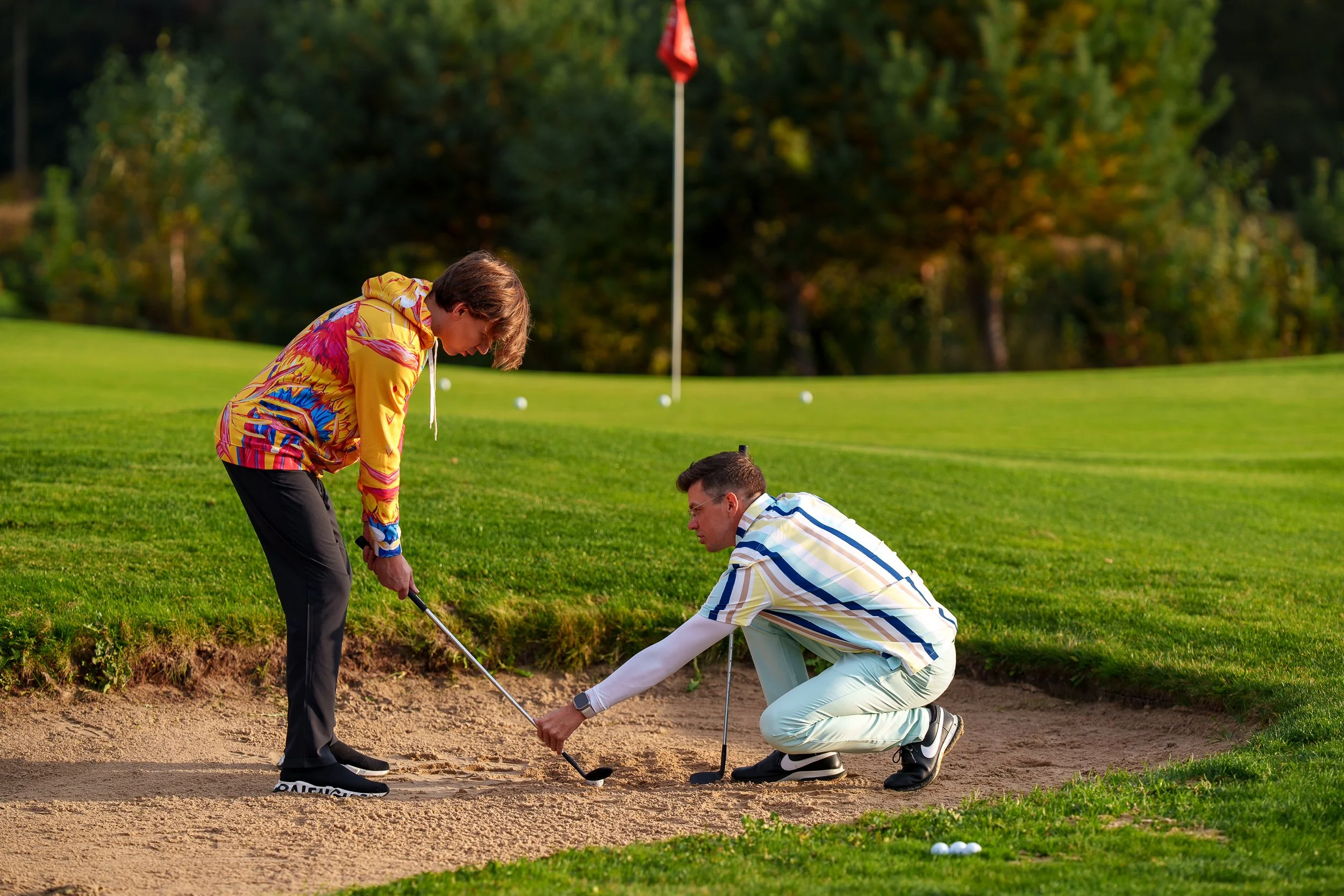 trener golfa poprawia pozycję ucznia grającego z bunkra