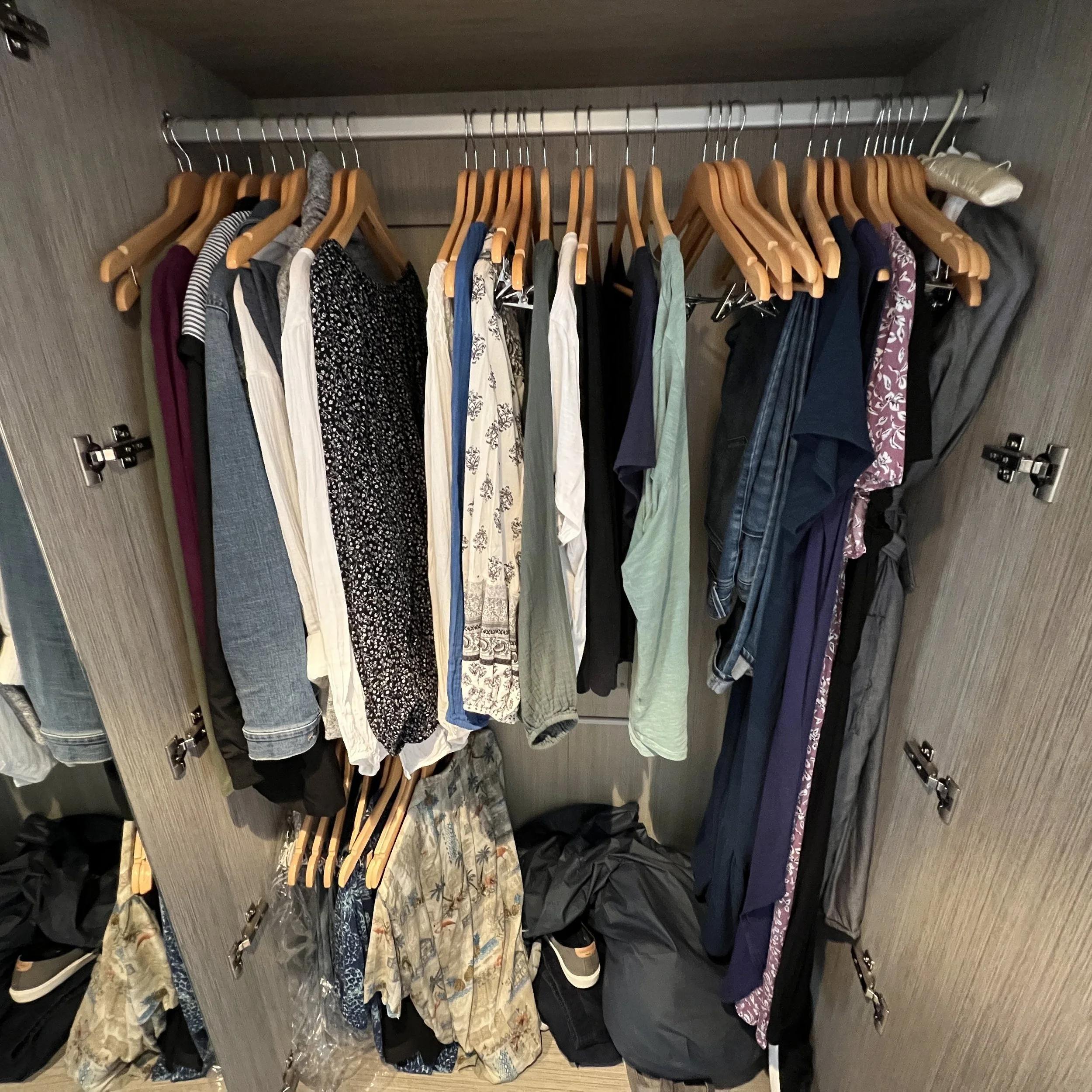 A shallow closet containing one full-length clothing rod and one half-length clothing rod below it. It contains the cruiser's clothing on wooden hangers.