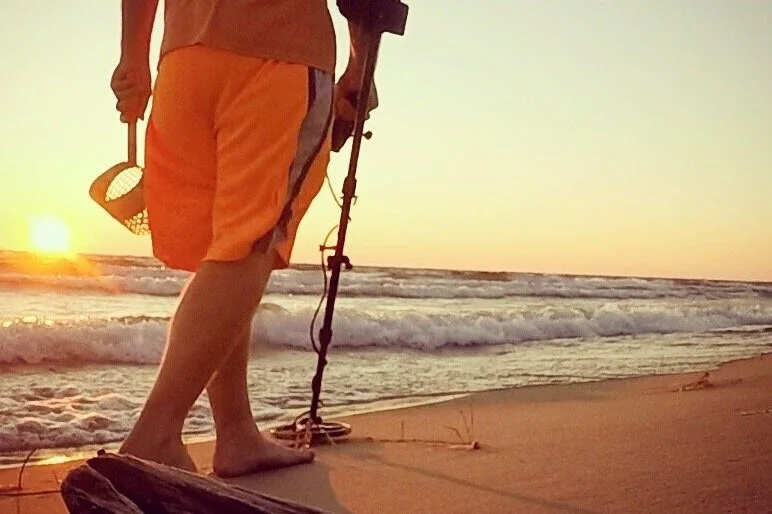 Walking in the sand with a metal detector at a beach during sunset with the waves crashing.