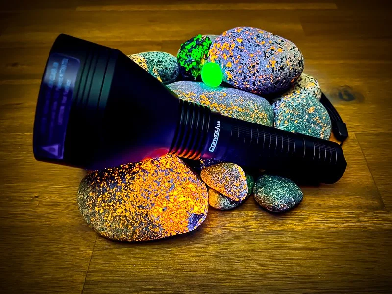 The Convoy L21B-X4 UV flashlight with Yooperlites and Uranium glass glowing underneath it.