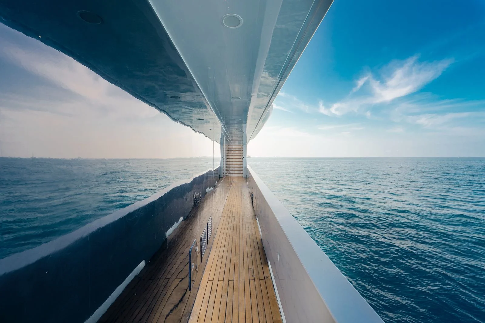 View from the side of a modern cruise ship looking out over calm ocean water with a partly cloudy sky in the background.