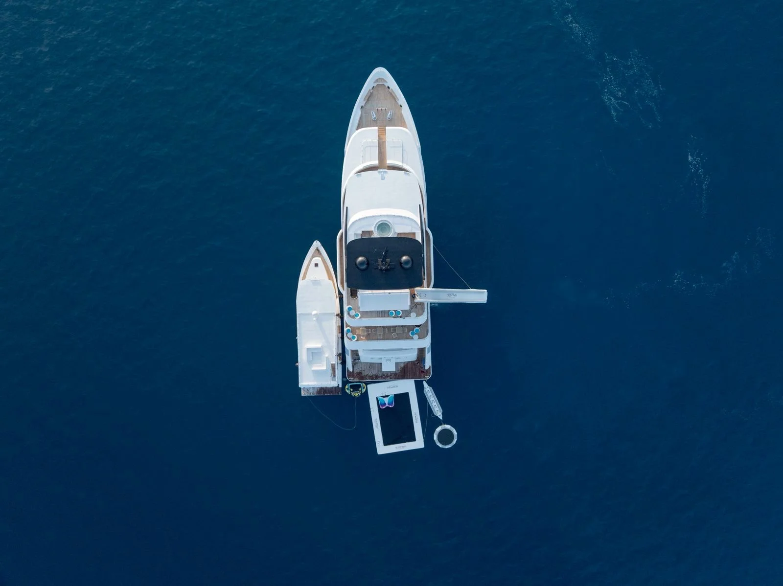 Overhead view of a white yacht anchored in deep blue water with a smaller boat attached to its side.