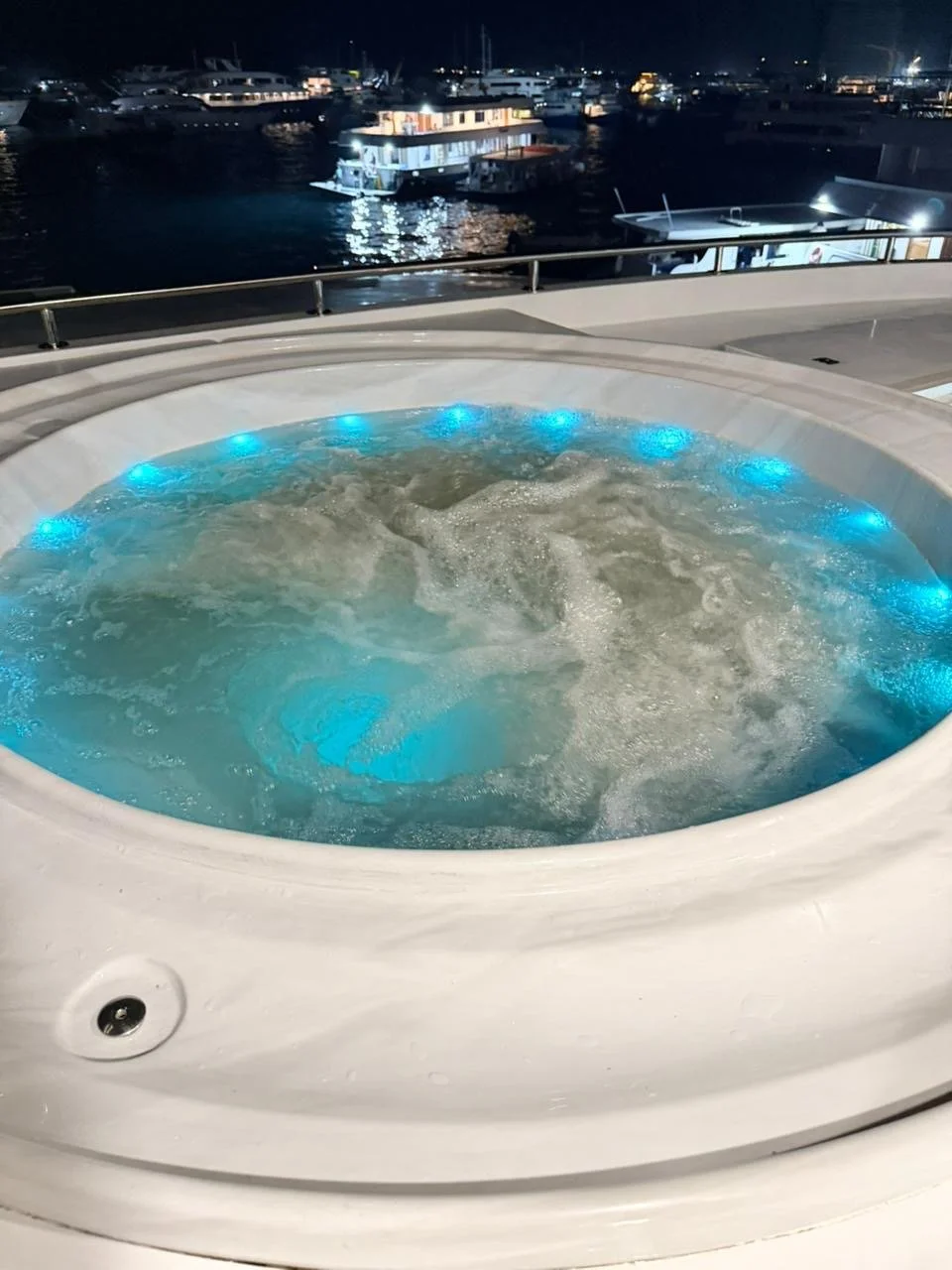 Jet hot tub on a yacht at night with boats and water in the background.