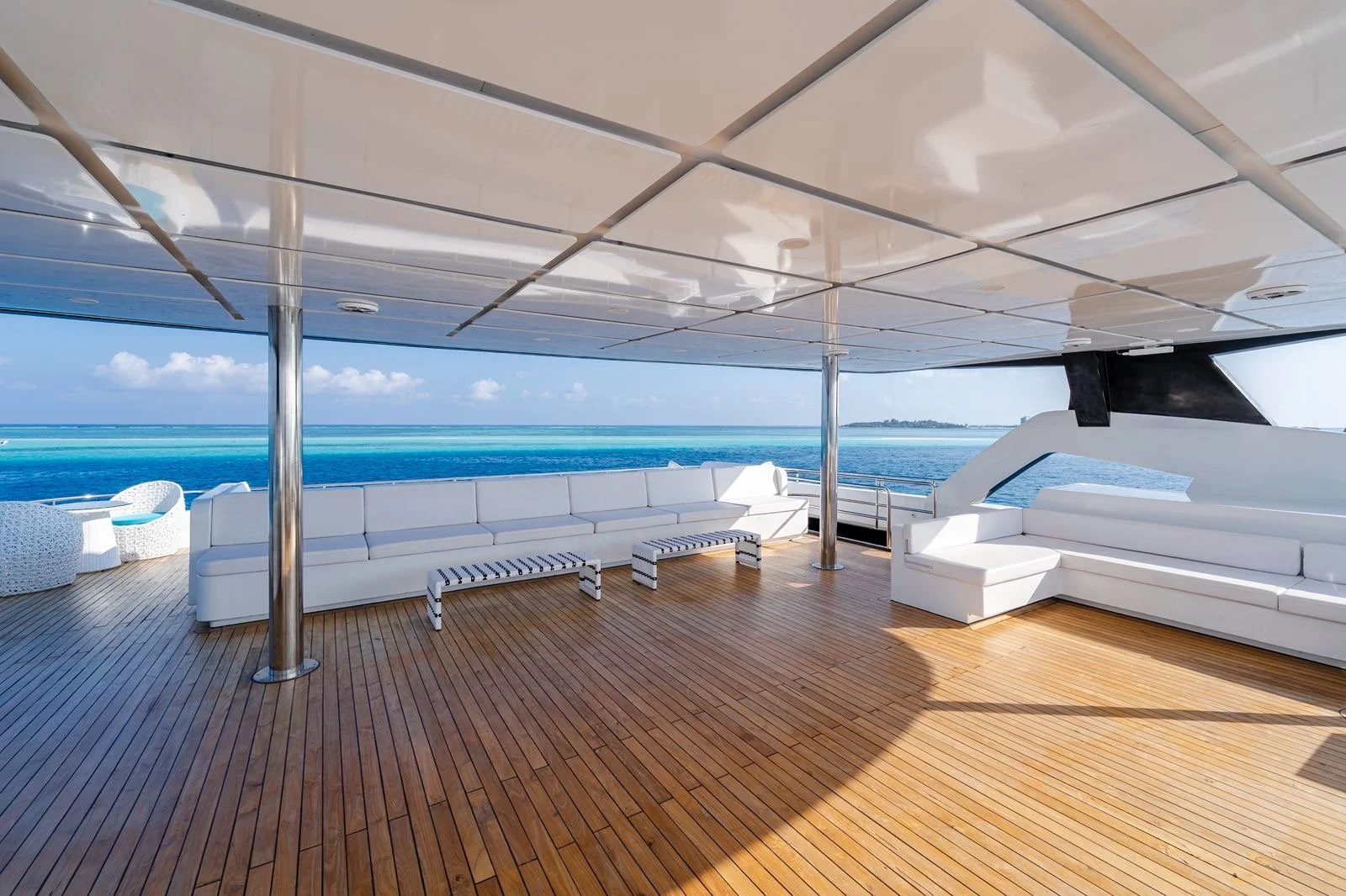 Outdoor deck area on a yacht with white seating, striped stools, and ocean view in the background.