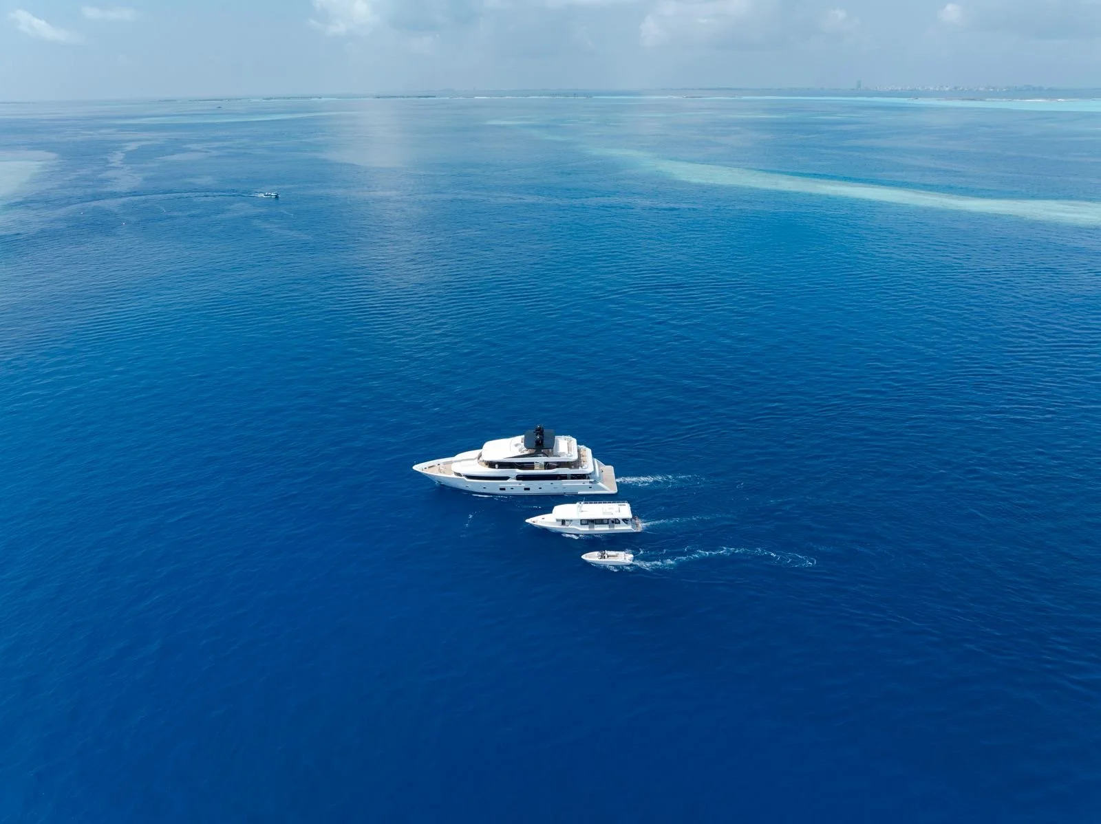 Multiple luxury boats sailing on calm blue ocean water, seen from above.