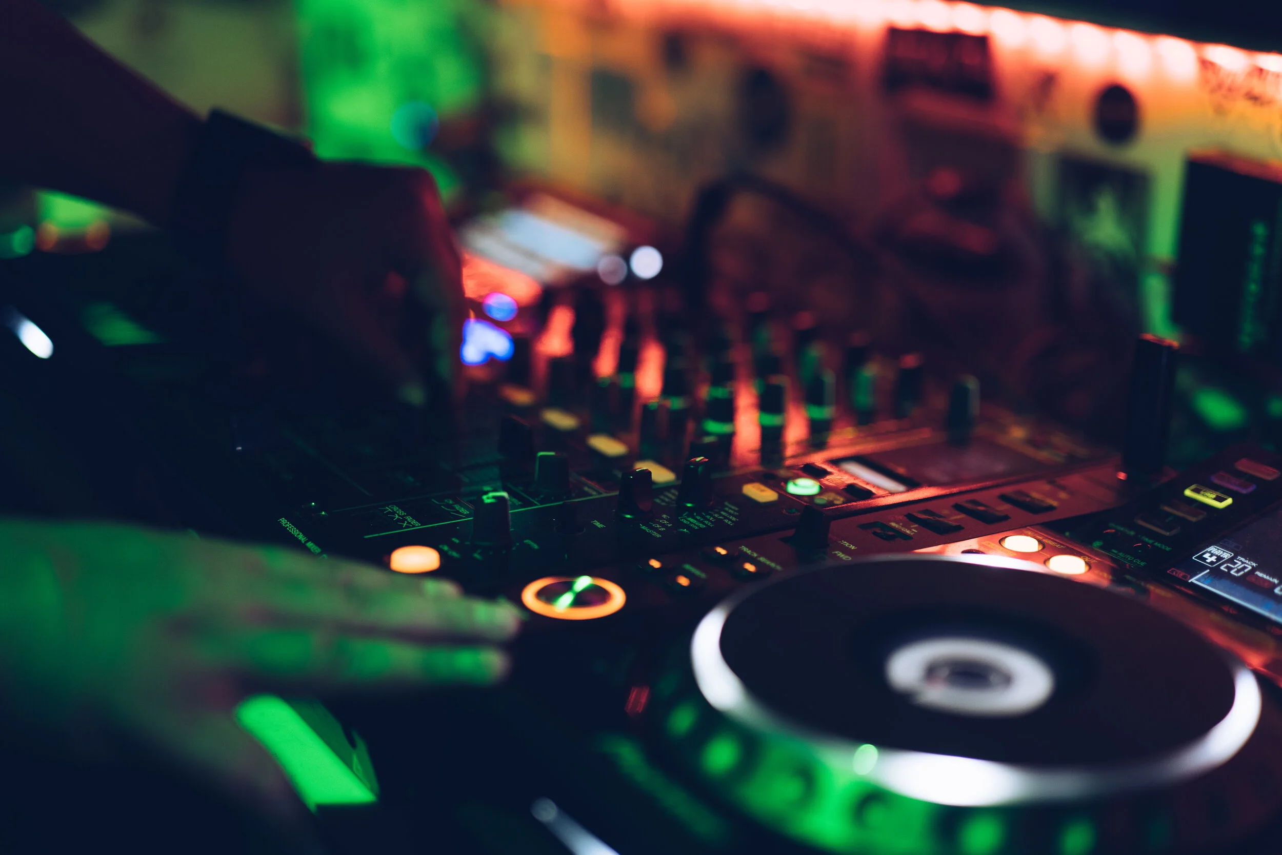 Close-up of a DJ's hand operating a DJ controller with colorful LED lights in a dimly lit setting.
