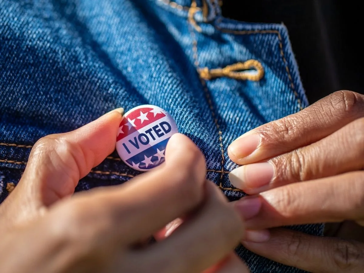 Person attaching an "I Voted" pin to a denim jacket that they are wearing.