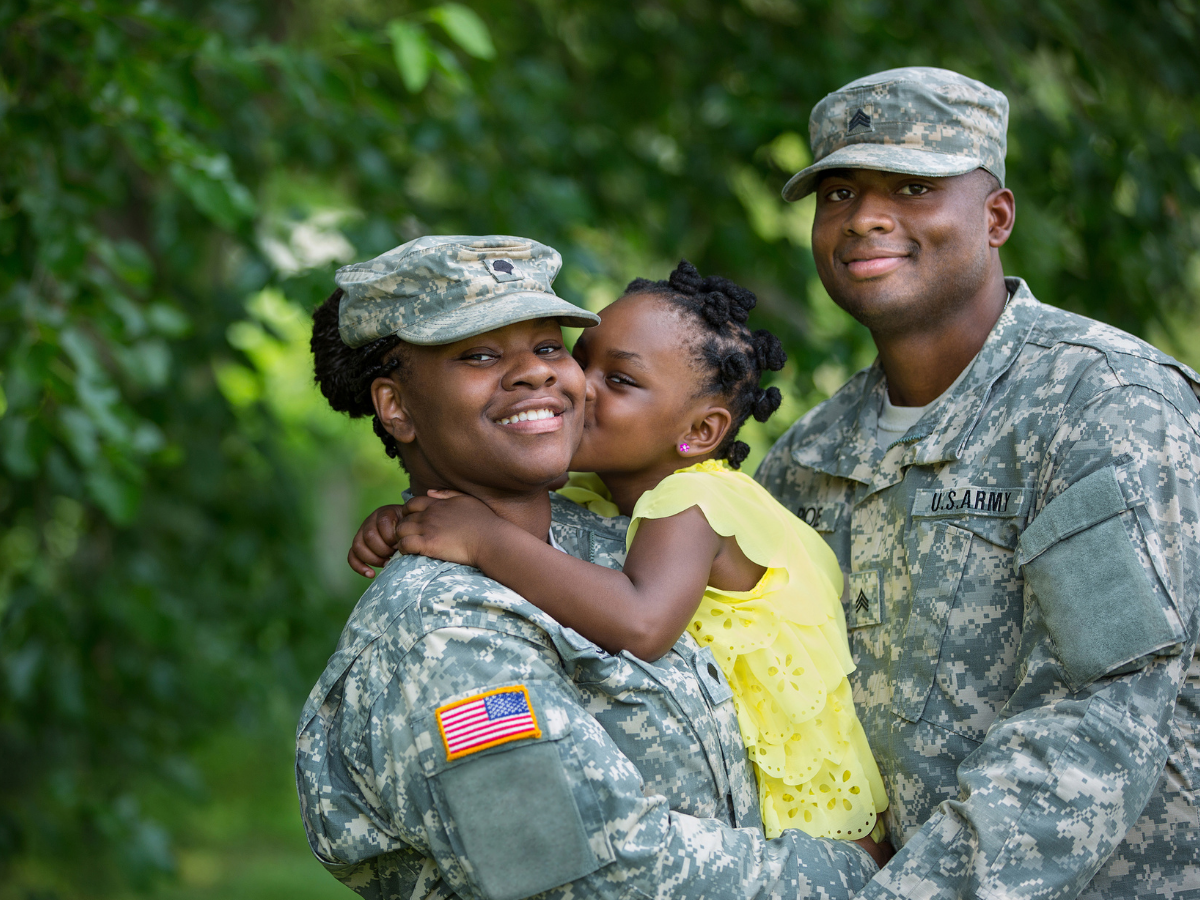 Woman and man in military camo holding a little girl in a yellow outfit