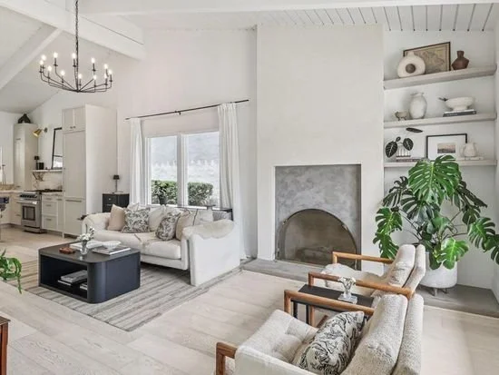 Bright living room with white walls, a white sofa, a black coffee table, a fireplace, and built-in shelves with decorative items and books.