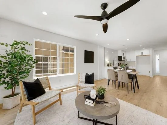 Modern living room and open kitchen with large window, ceiling fan, and minimal decor