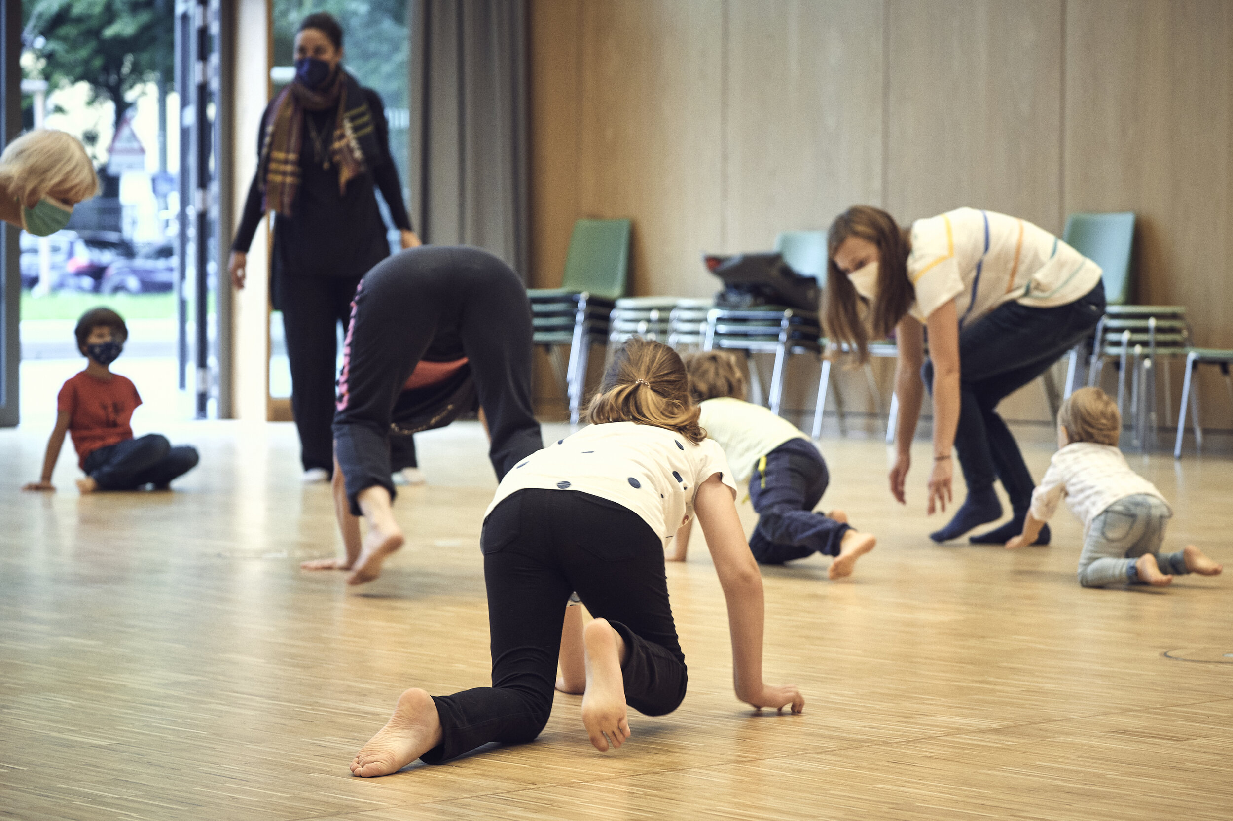  Situation aus dem Programmpunkt “Tanzen für alle” im Saal der Luise. Kinder und Erwachsene jeden Alters in Bewegung, teils auf dem Boden, teils stehend.  