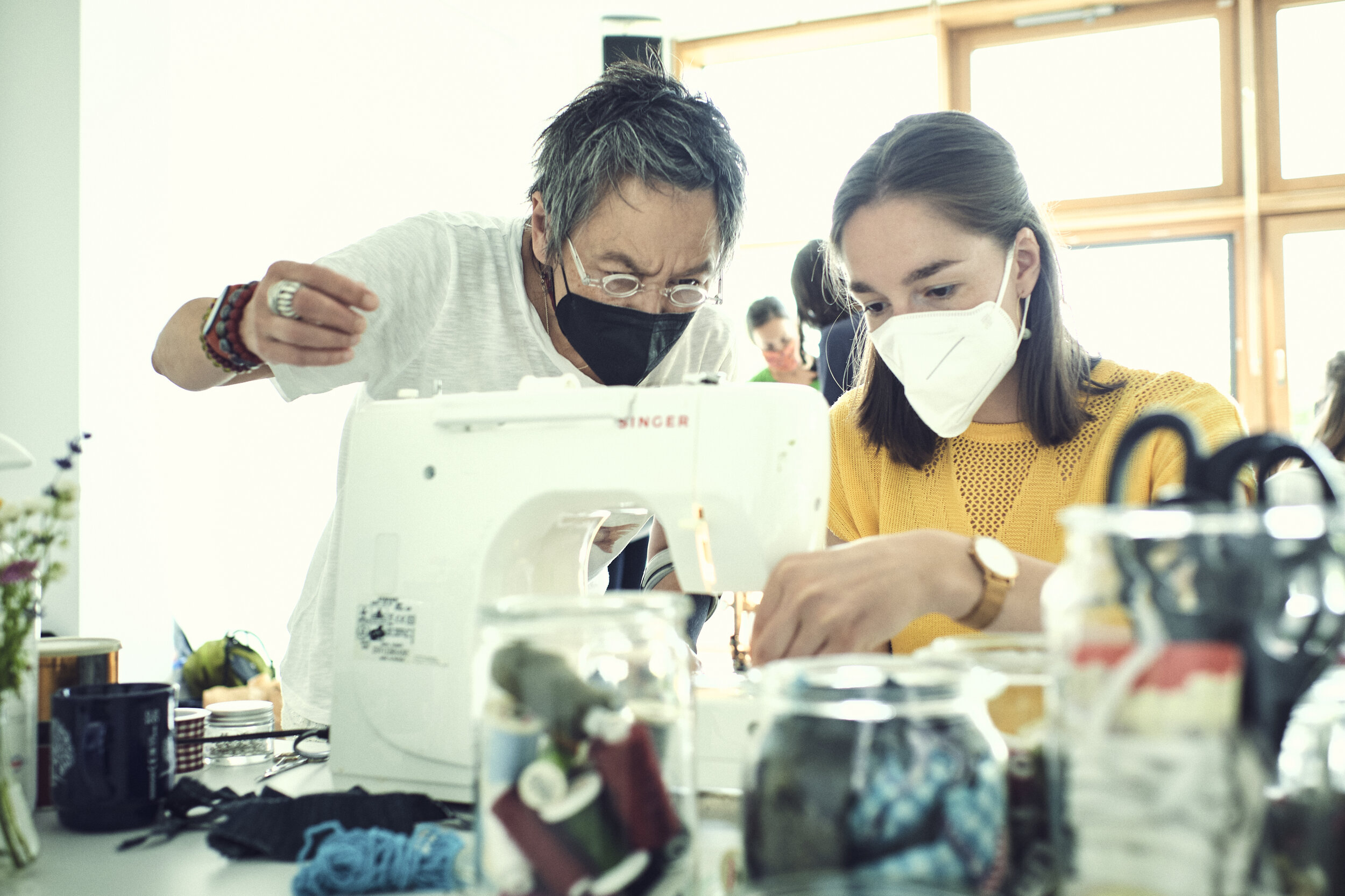  Eine Ehrenamtliche zeigt einer Frau, wie sie die eben ertauschte Kleidung umnähen kann. Man sieht die beiden konzentriert hinter der Nähmaschine. 