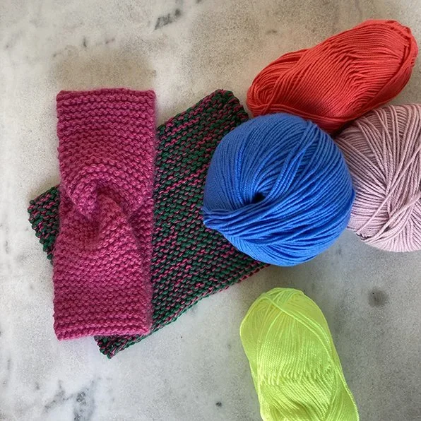 Wollknäuel in verschiedenen Farben. Zwei gestrickte Stirnbändern rosa und grün.