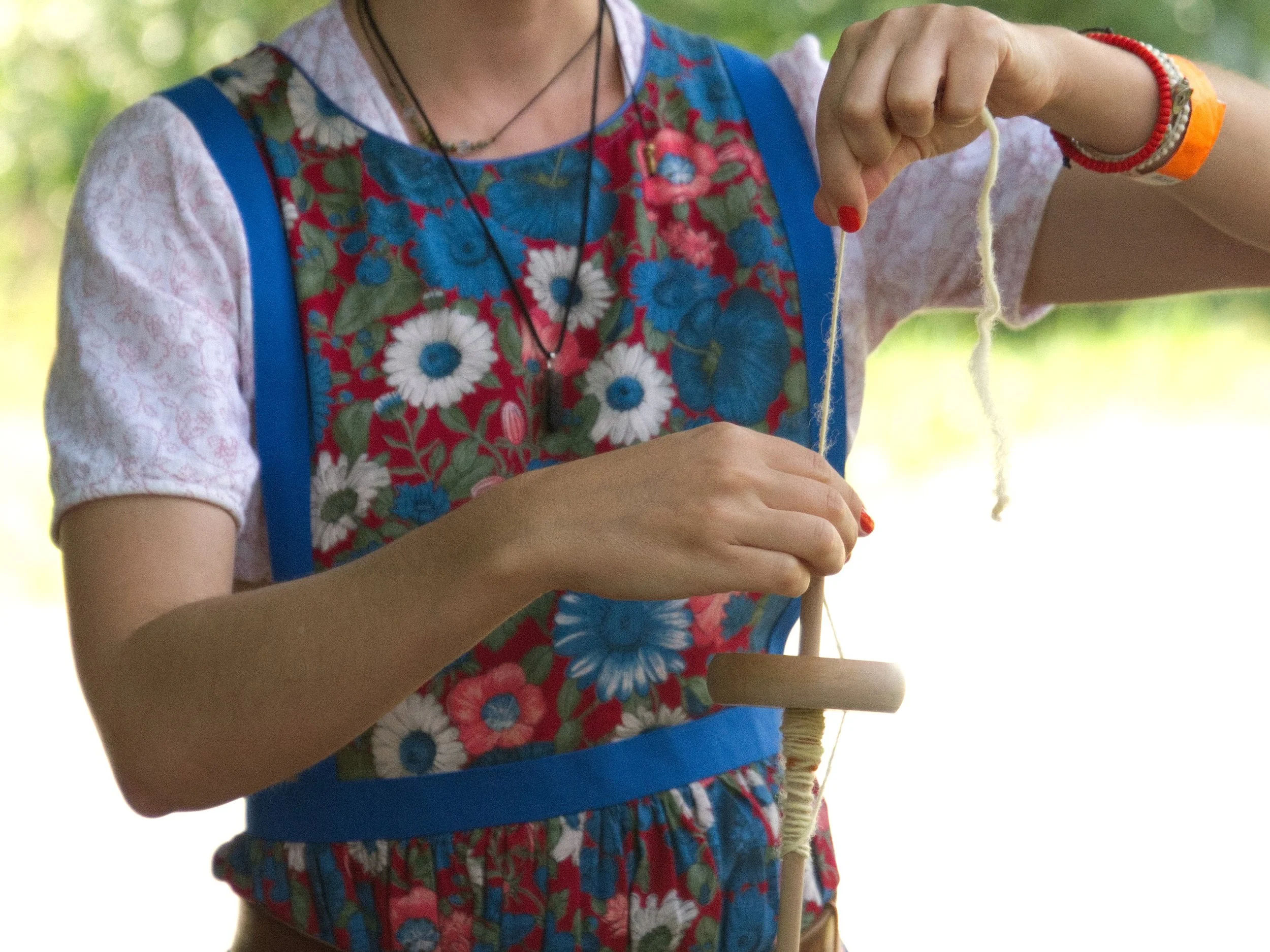 Eine Person mit buntem Kleid beim Fadenspinnen mit einer Handspule