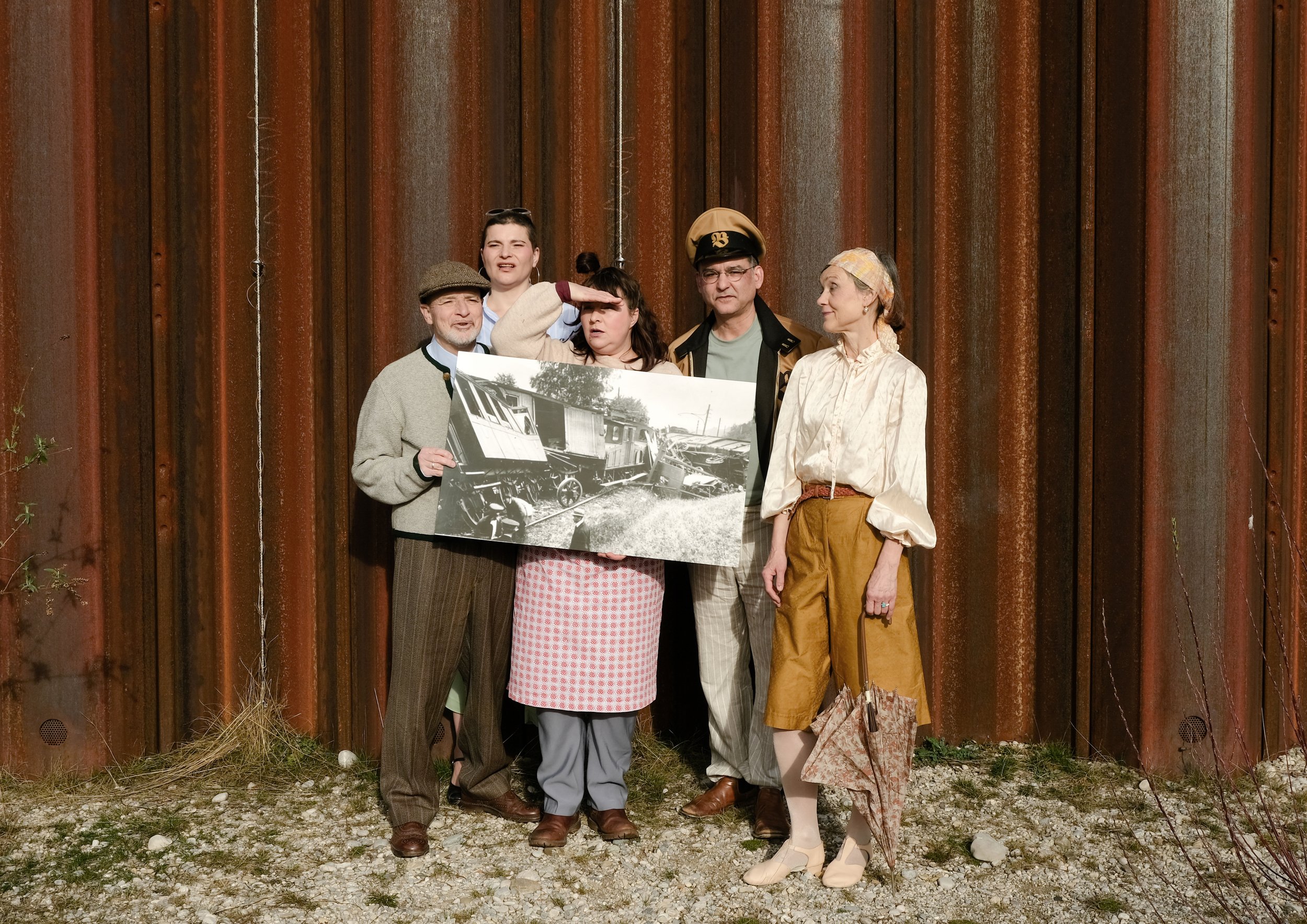 Foto. Fünf Schauspieler:innen mit einem schwarz weißen Bild in der Hand.