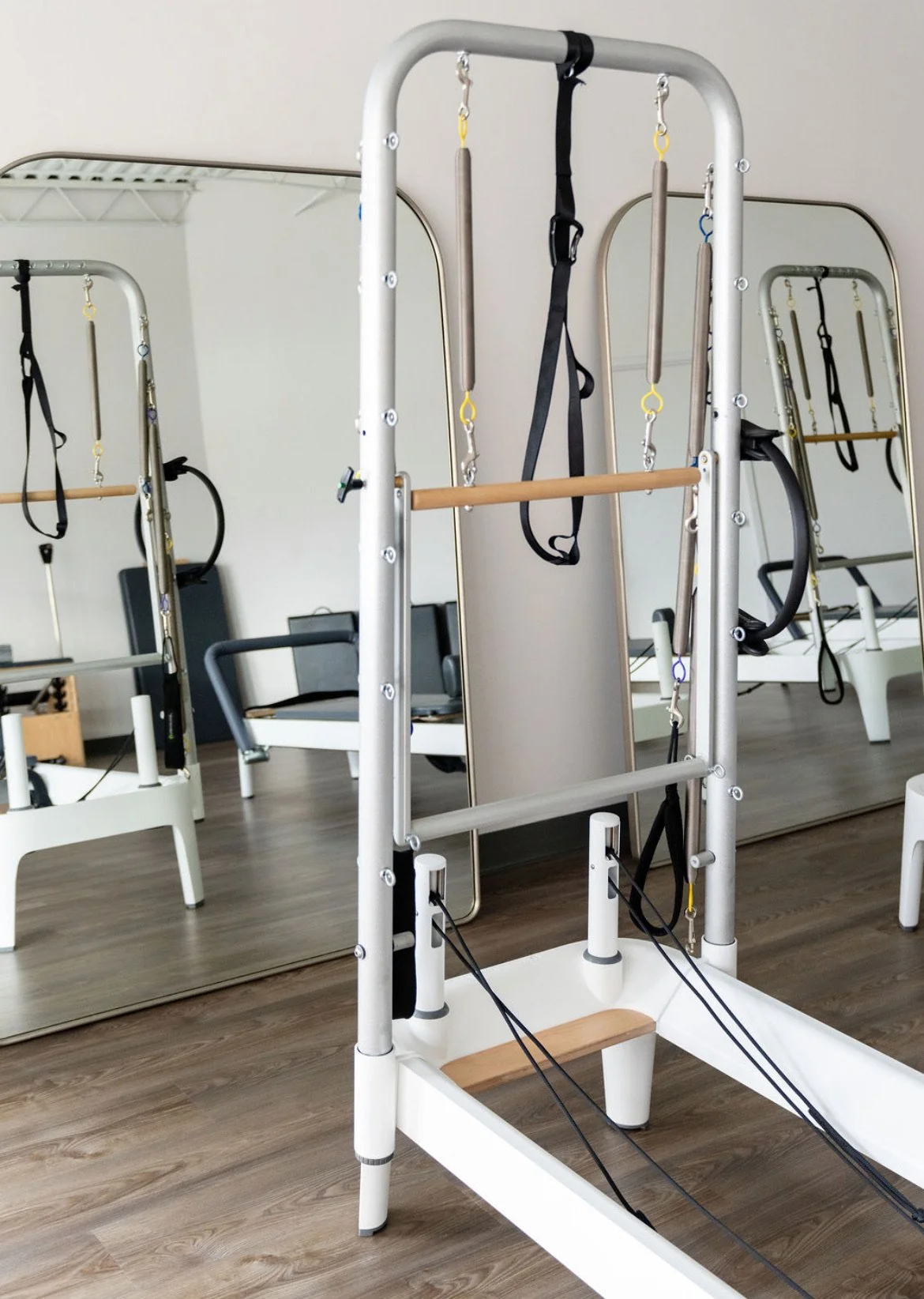 A woman in red workout clothes is performing a yoga pose on a mat, with her upper body arched backwards and her hands holding onto a bar above her head. The photo is taken from a low angle, capturing her from ground level, with part of another person in white socks in the foreground.