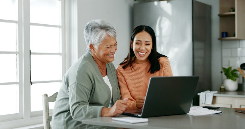 Mother with adult daughter, smiling looking at laptop, notebooks in family home