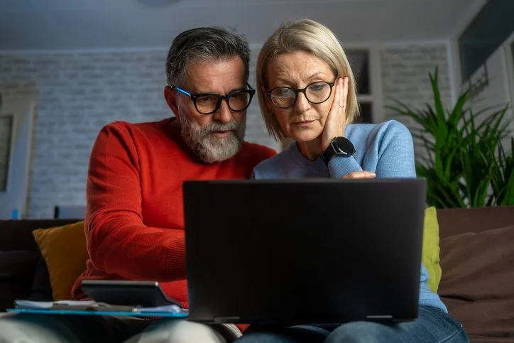 Couple looking at paperwork, calculator, and laptop, looking concerned