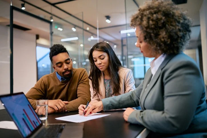 Young couple talking to a financial advisor and signing documents in an office.