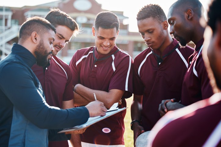 A group of college athletes in uniform talking to their coach